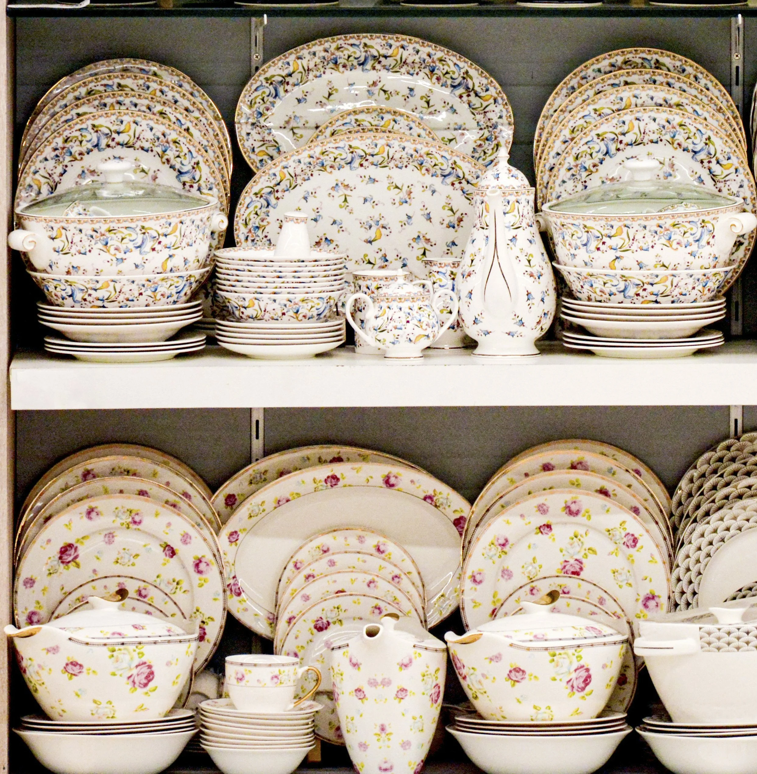 Display of floral patterned dinnerware including plates, bowls, cups, and serving dishes on shelves in a store.