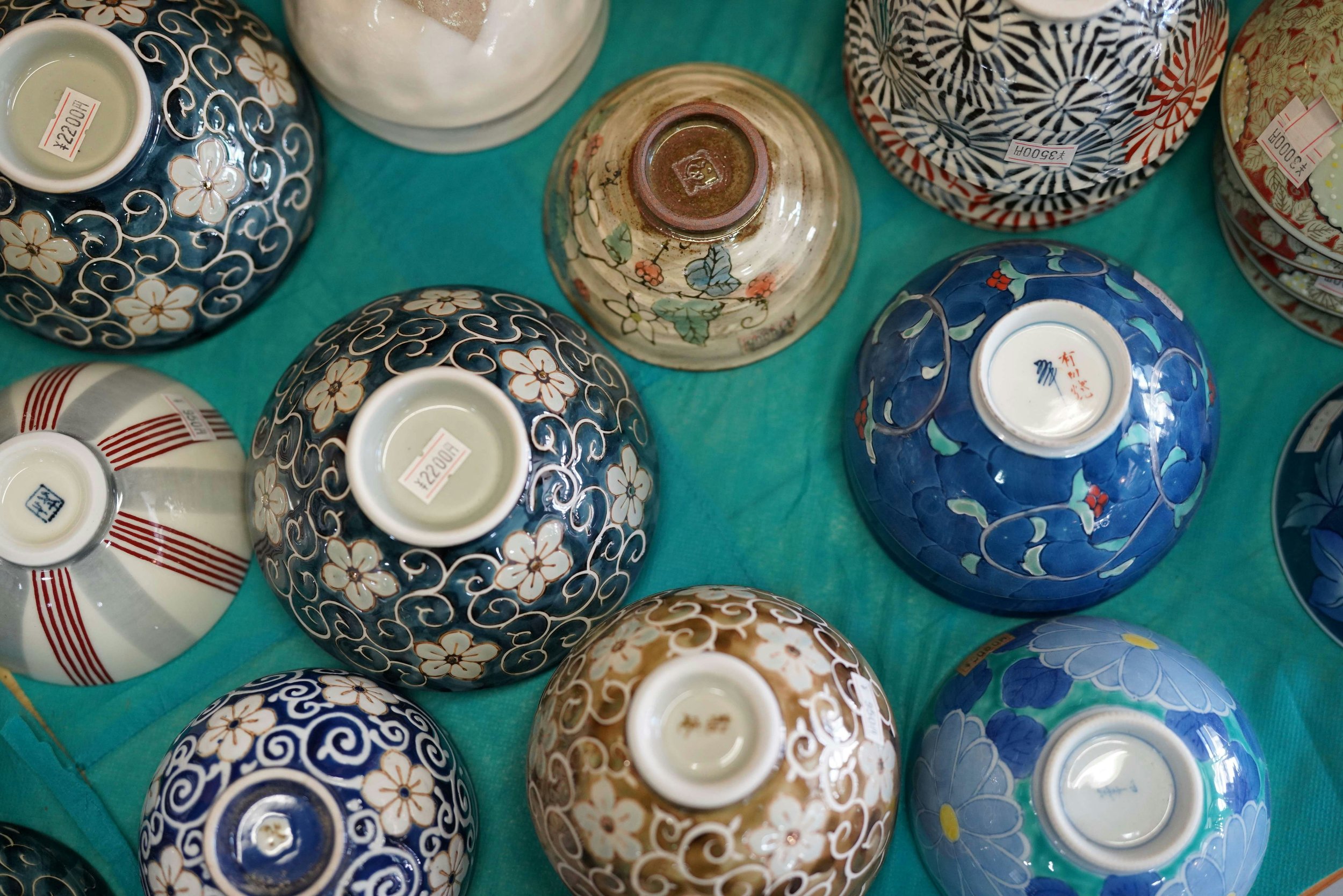 Multiple decorative ceramic bowls with intricate floral and geometric patterns in colors such as blue, white, red, and gold, displayed upside down on a teal surface.