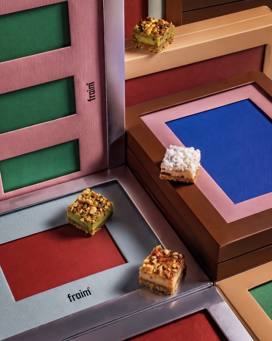 Four pieces of assorted dessert placed on colorful chocolate tasting boxes with the brand name 'fraim' printed on them.