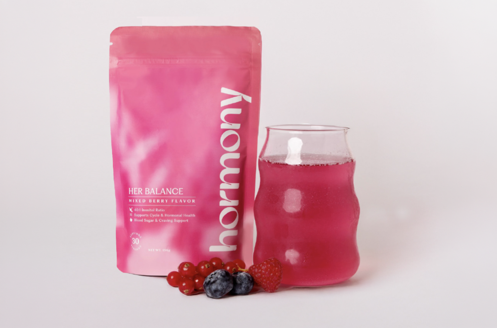 Pink powder packet labeled "Her Balance" with mixed berry flavor, a glass of pink berry drink, and fresh berries including blueberries, raspberries, and red currants on a white background.