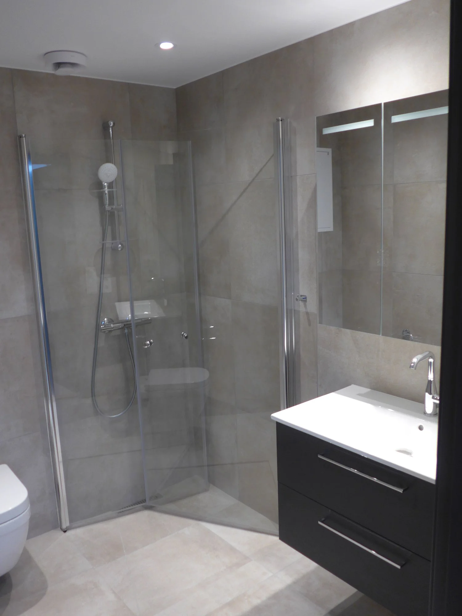 Contemporary bathroom with glass-enclosed shower, beige tiled walls and floor, white sink with black vanity, and mirror.