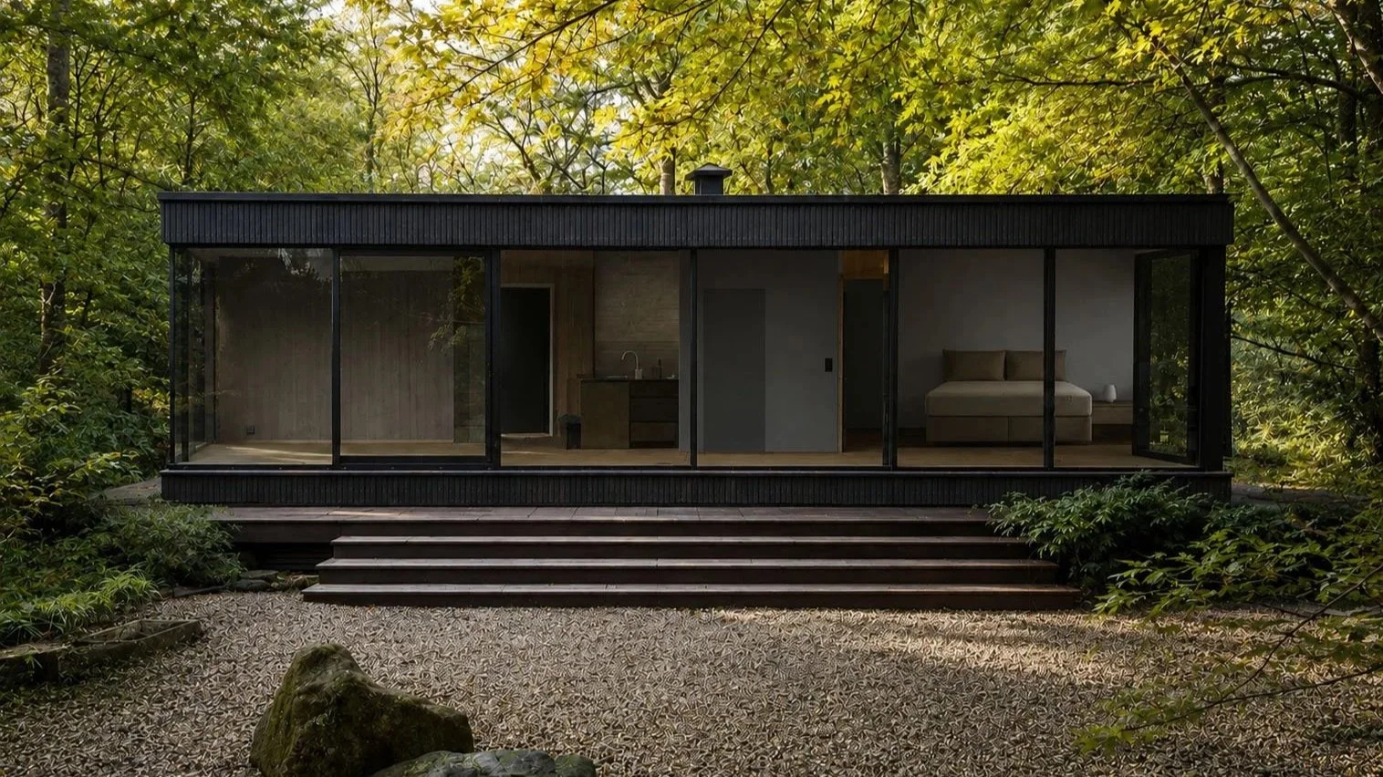 Modern glass house surrounded by lush green trees, with a gravel area in front and steps leading up to the entrance.