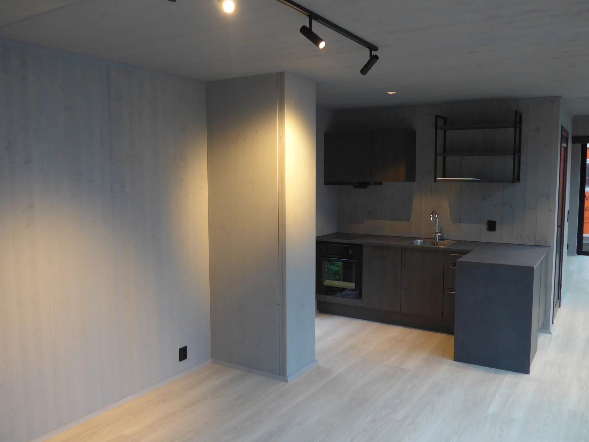 Modern kitchen with grey cabinets, a black range hood, and a grey countertop, illuminated by ceiling track lighting.