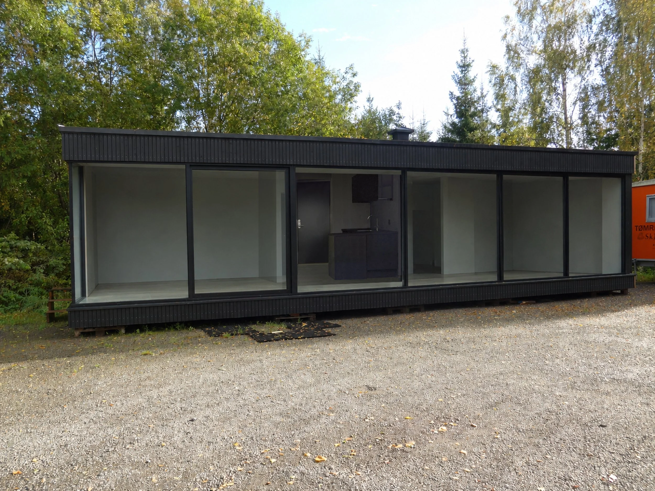 Modern black-framed glass building with sliding doors, surrounded by greenery and trees, indicating an outdoor setting.