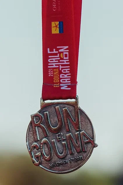 A finisher's medal with a red ribbon that reads '2021 El Coqui 4 MARCHA, 2021,' attached to a metal medal inscribed with 'RUN EL GOUNA' and the date 'November 7th, 2021.'