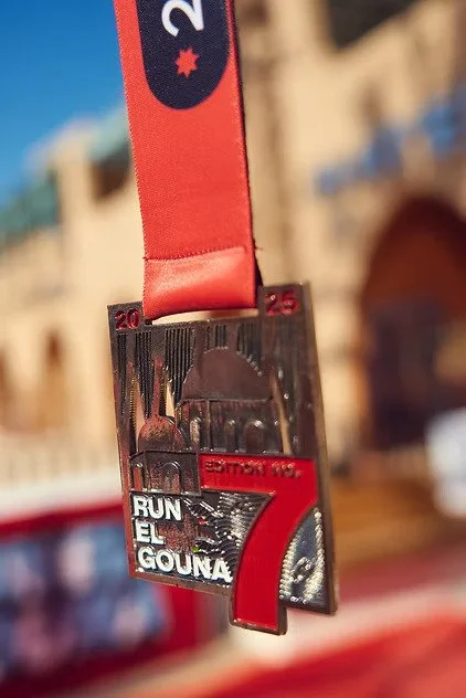 Medal with a red ribbon, engraved with 'Run El Gouna' and the number 7, hanging upside down.