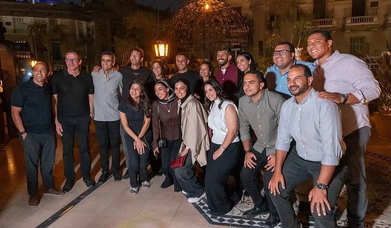 Group of 15 people, mostly young adults, smiling and posing together outdoors at night.