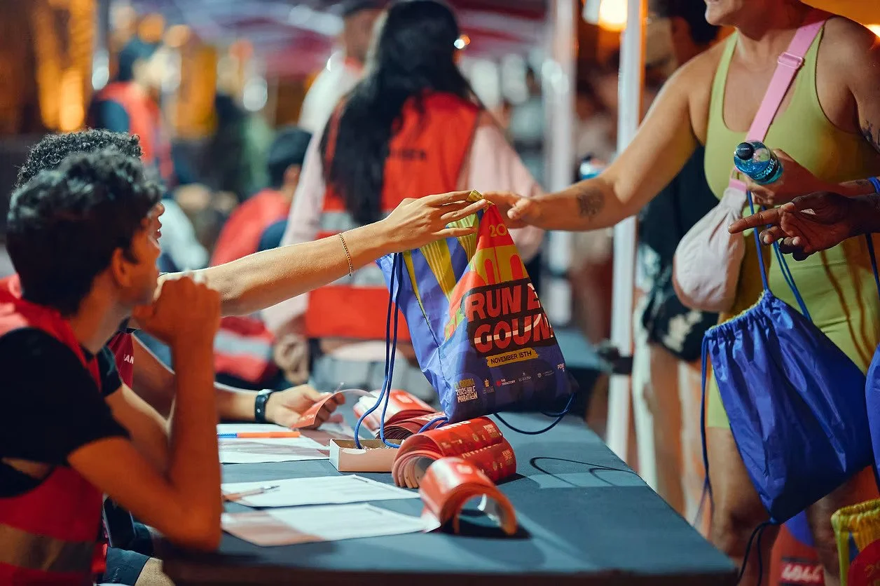People exchanging race bibs at a registration table at night, likely before a running event.