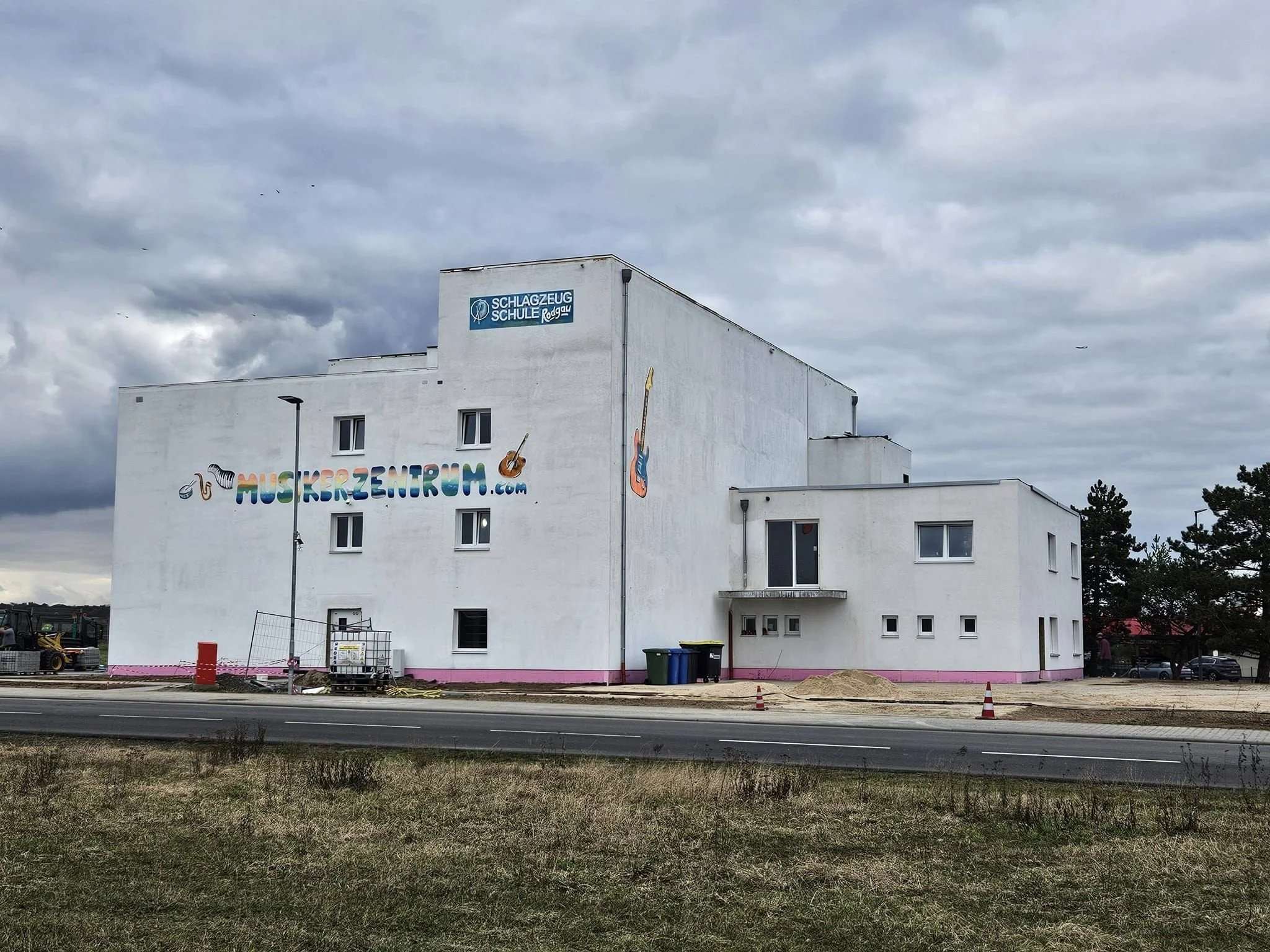 Ein weißes mehrstöckiges Gebäude mit bunten Graffiti-Schriftzug und Musiknoten. Ein Schild oben auf dem Gebäude zeigt den Namen 'Schlagzeug Schule Rodgau'.