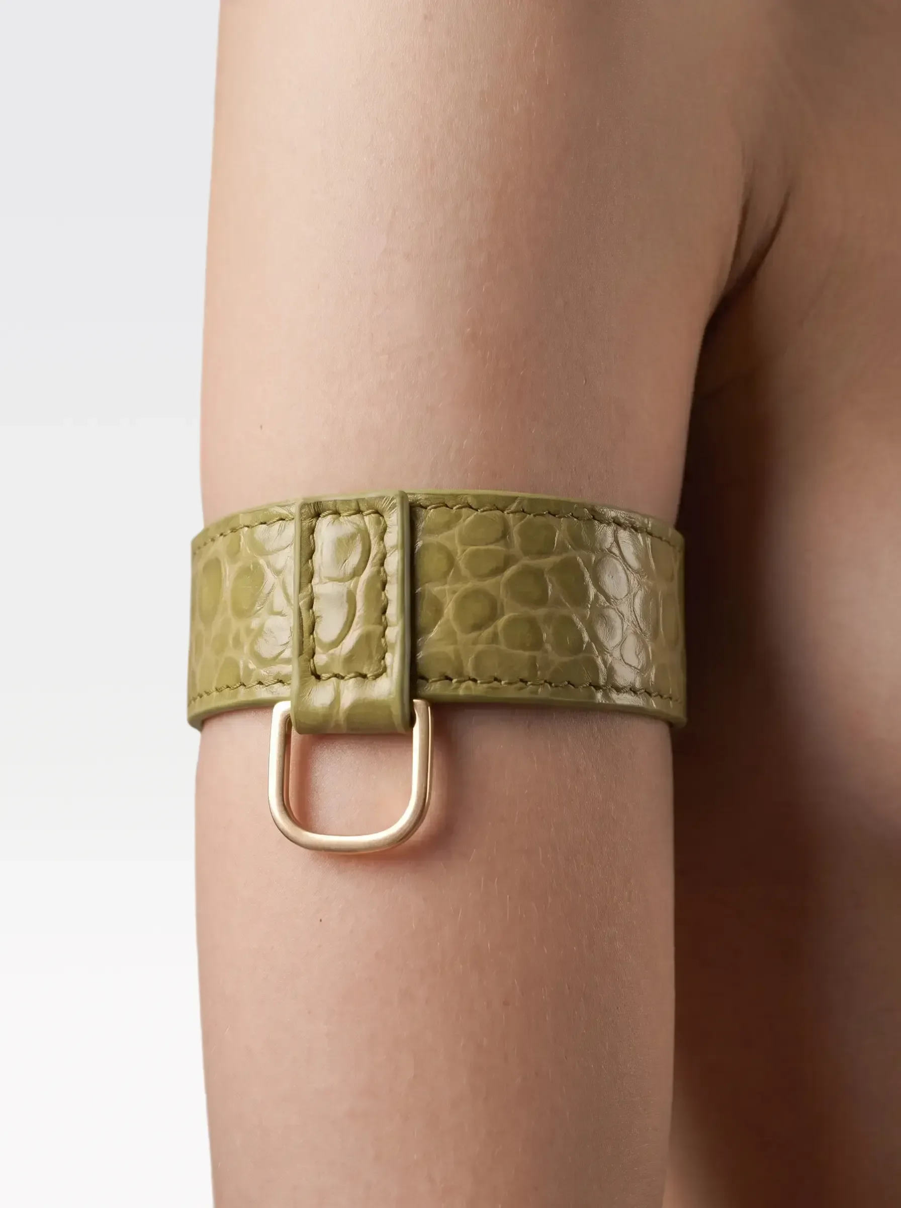 Sainte Sve Arm Bracelets Croc in pistachio crocodile-embossed lambskin with a 24K gold-plated brass D ring, worn on the upper arm, editorial image