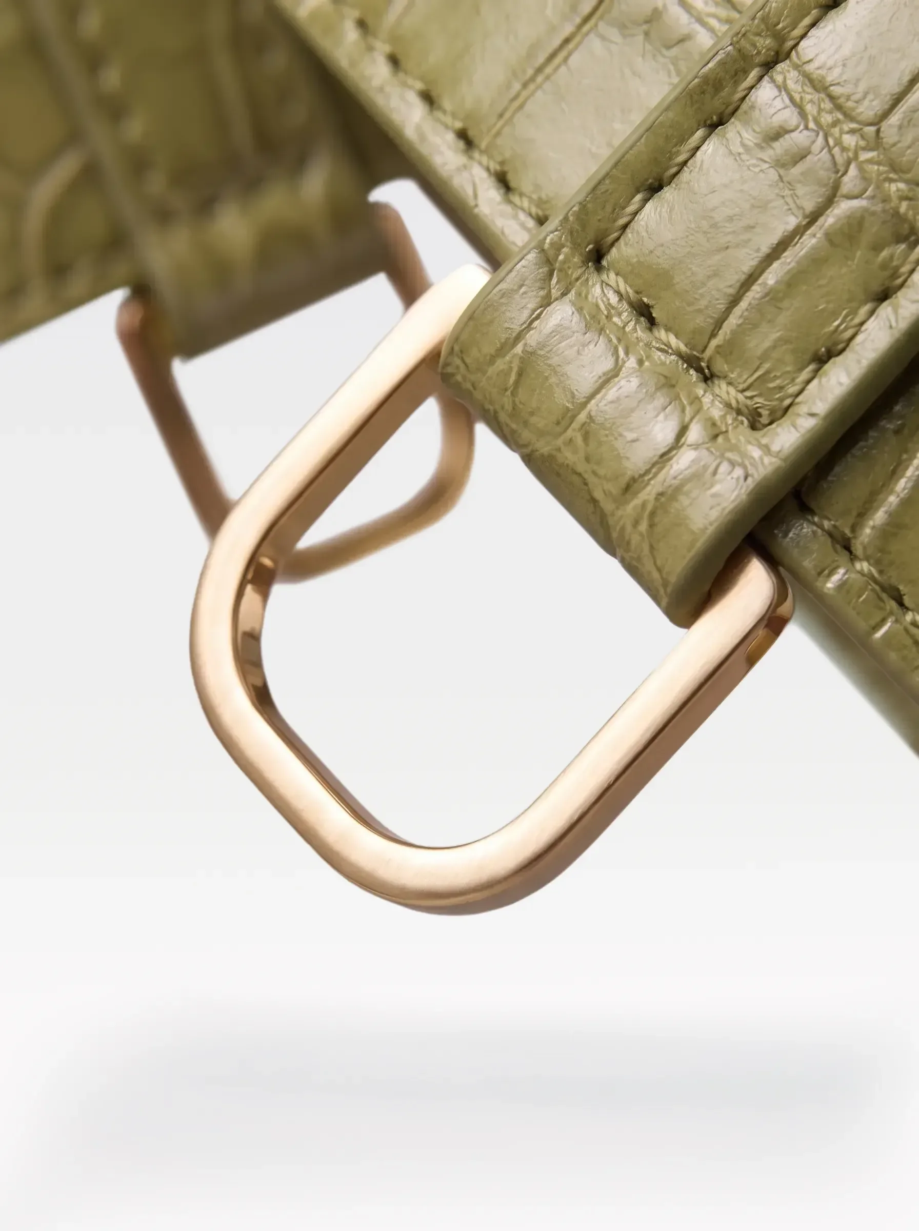 Close-up of the 24K gold-plated brass D ring on a pistachio crocodile-embossed lambskin garter by Sainte Sve
