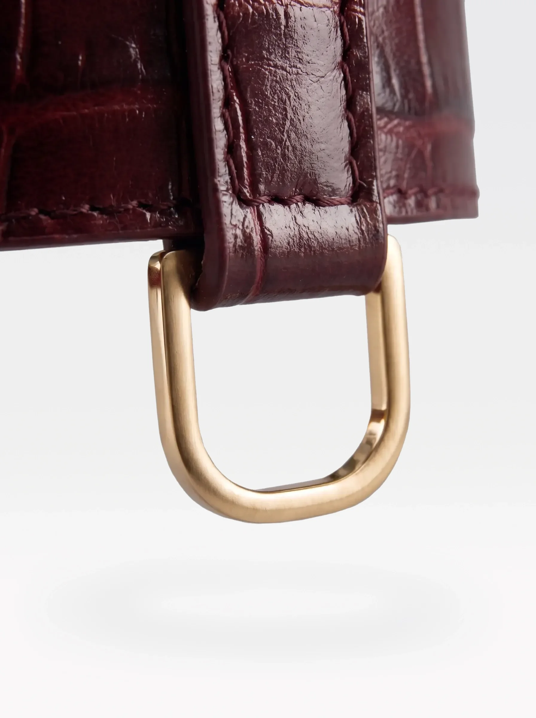 Close-up of the 24K gold-plated brass D ring on a burgundy crocodile-embossed lambskin choker by Sainte Sve