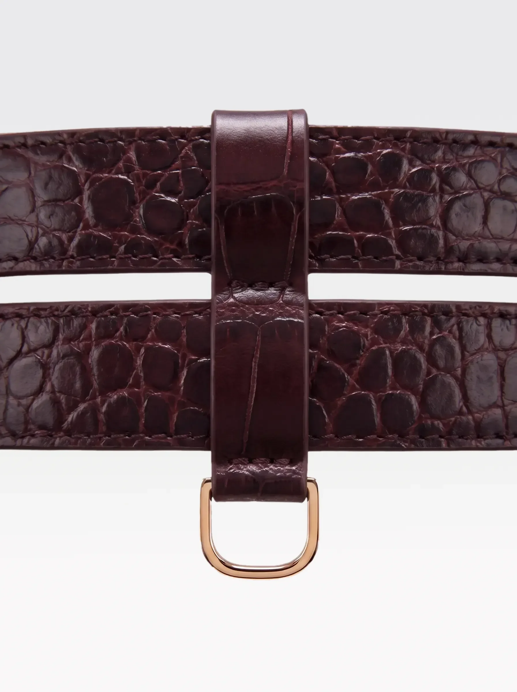 Close-up of the 24K gold-plated brass D ring on the burgundy crocodile-embossed lambskin double band of the Sainte Sve Belt Croc