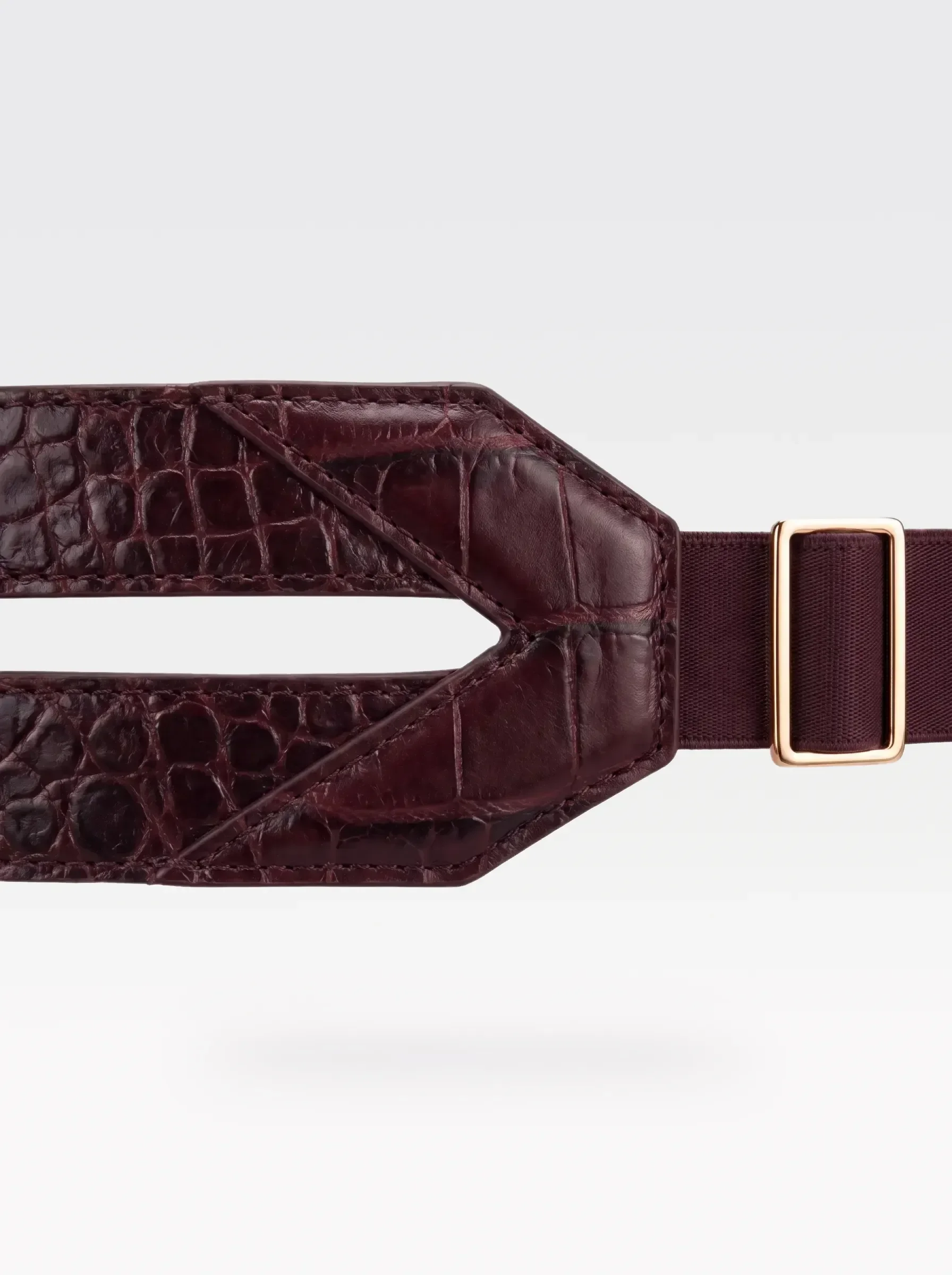 Close-up of the V-shaped burgundy crocodile-embossed lambskin panel and 24K gold-plated brass slider of the Sainte Sve Belt Croc