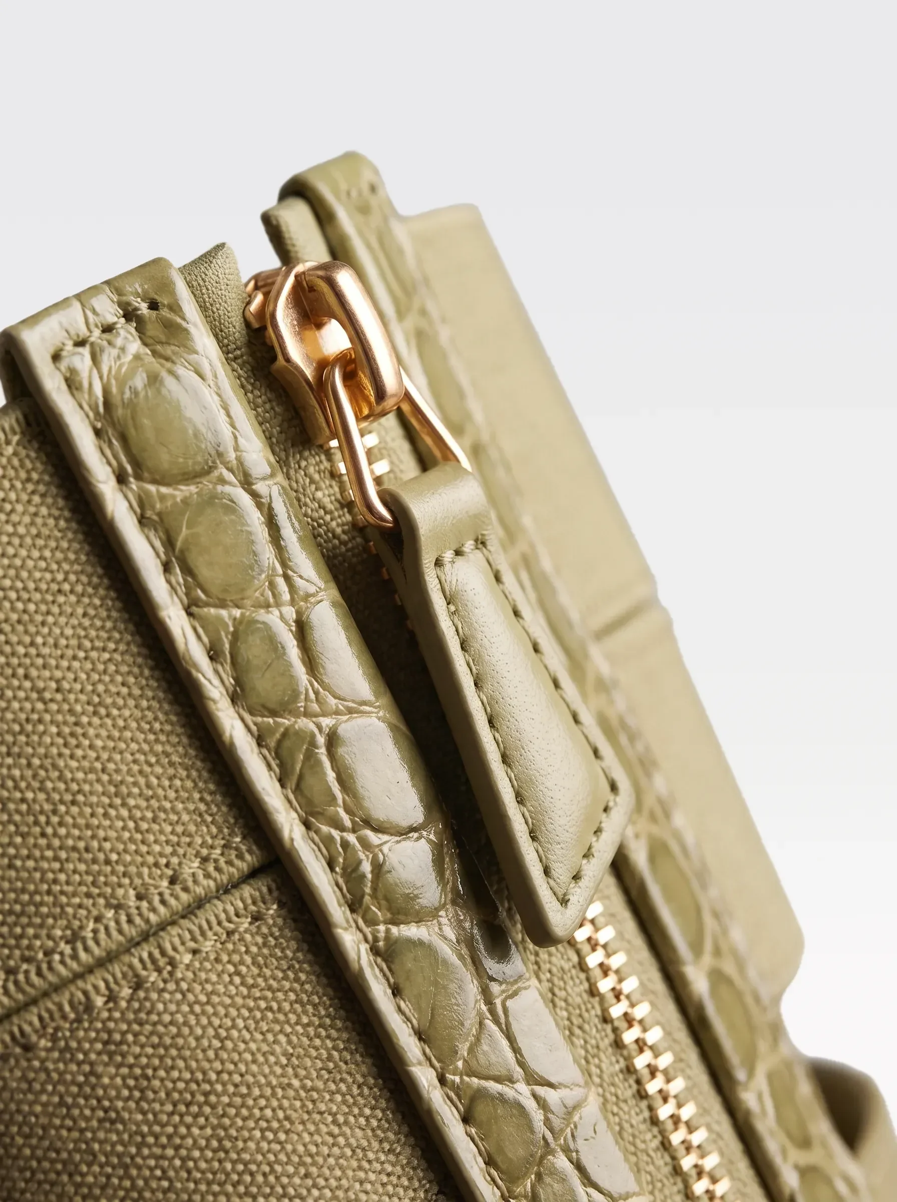 Close-up of the 24K gold-plated brass zip on the pistachio crocodile-embossed lambskin of the Sainte Sve V.N.V Croc