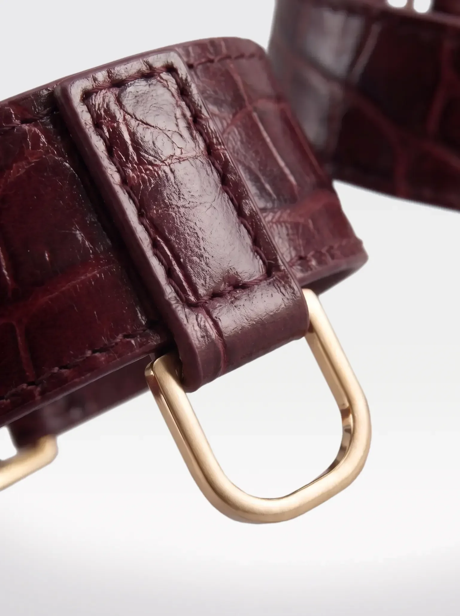 Close-up of the 24K gold-plated brass D ring on a burgundy crocodile-embossed lambskin ankle bracelet by Sainte Sve