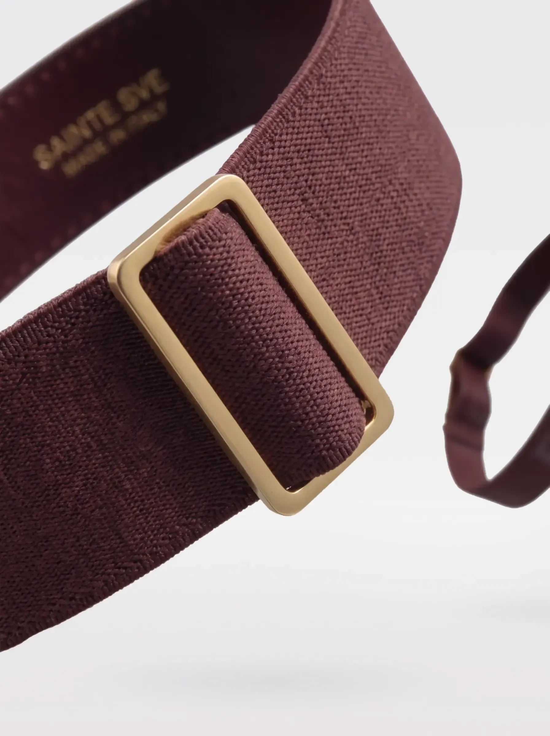 Close-up of the 24K gold-plated brass slider on the burgundy elastic band of a Sainte Sve Garters Croc