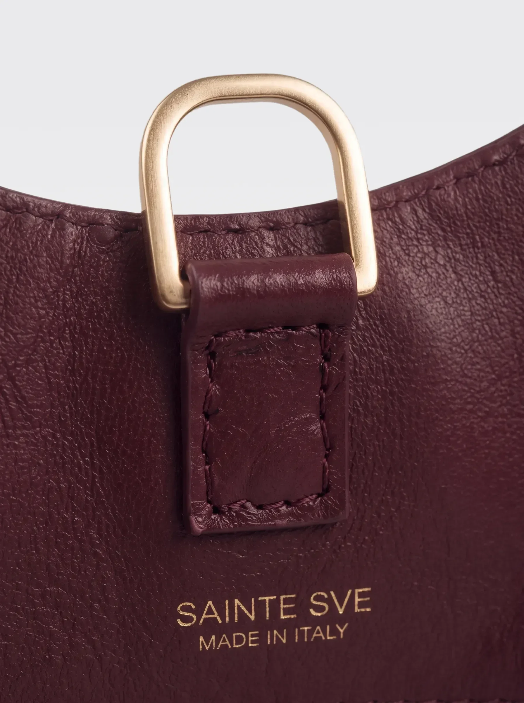 Close-up of the 24K gold-plated brass D ring and the foil-stamped Sainte Sve Made in Italy logo on the burgundy lining of the Sainte Sve V.N.V Croc