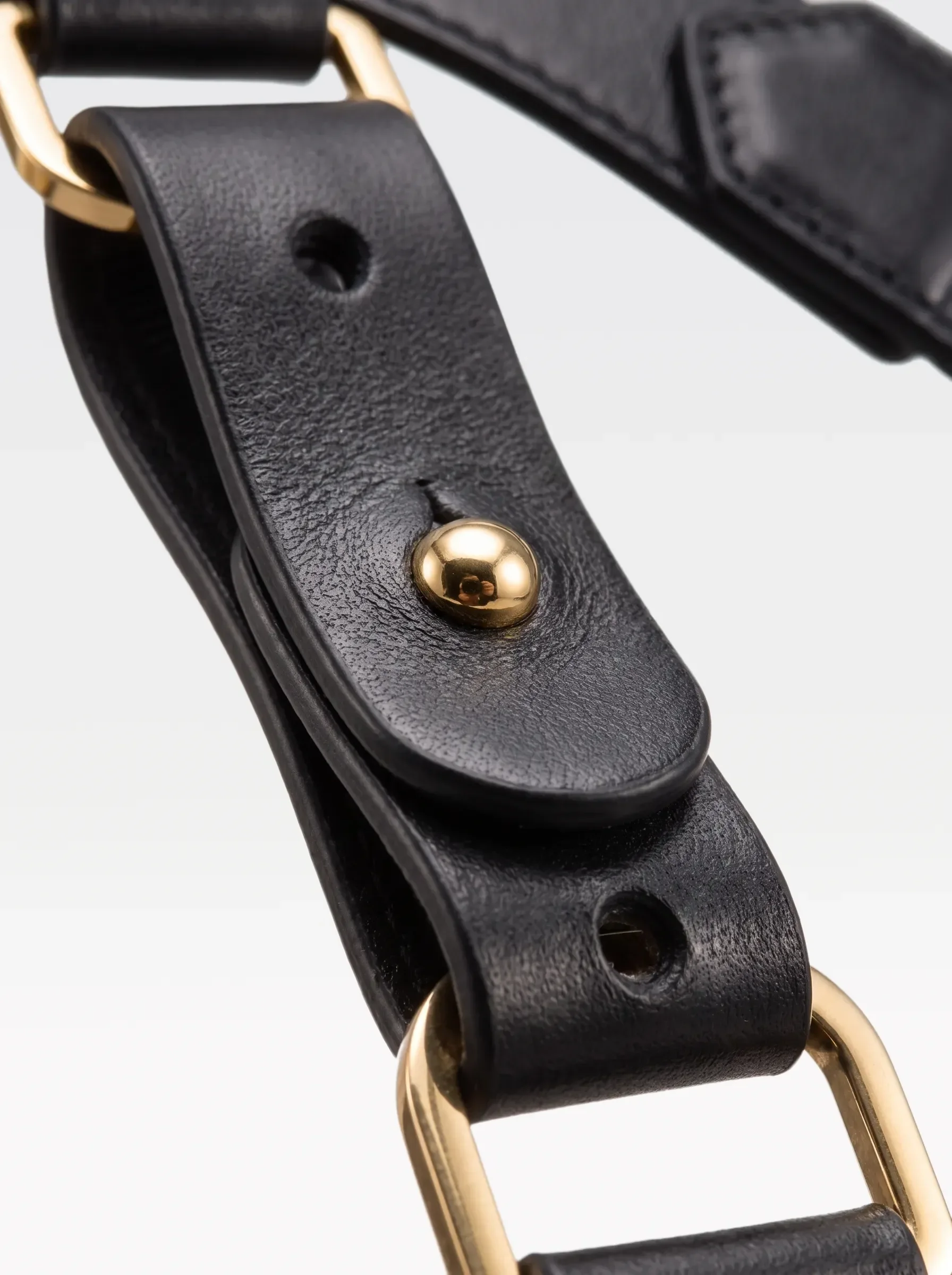 Close-up of the 24K gold-plated brass connector rivet and D ring on the black nappa lambskin strap of the Sainte Sve Belt Plus Nappa