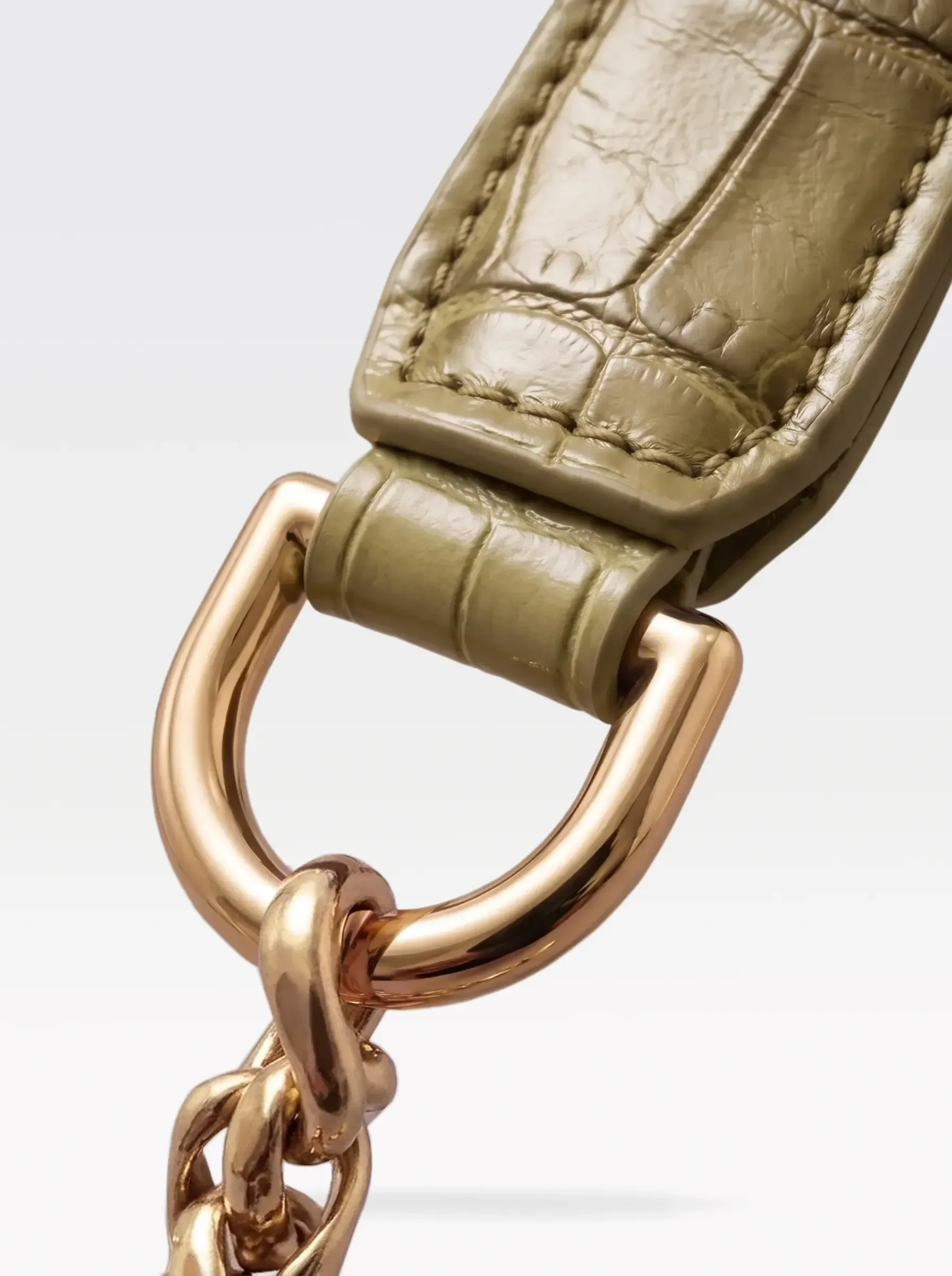 Close-up of the 24K gold-plated brass D ring joining the pistachio crocodile-embossed lambskin handle to the chain of the Sainte Sve Leash Croc