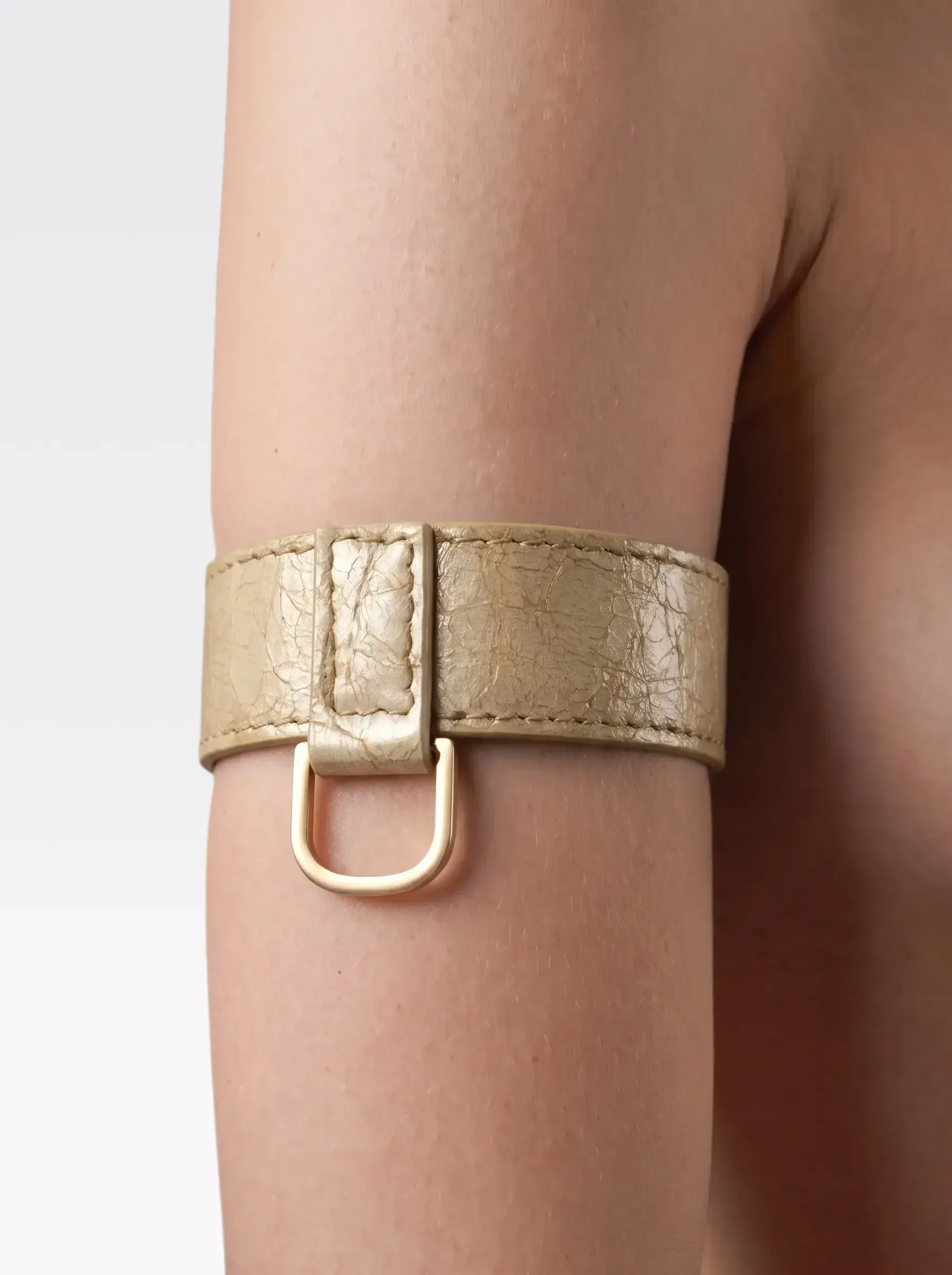 Sainte Sve Arm Bracelets Laminated in gold laminated lambskin with a 24K gold-plated brass D ring, worn on the upper arm, editorial image