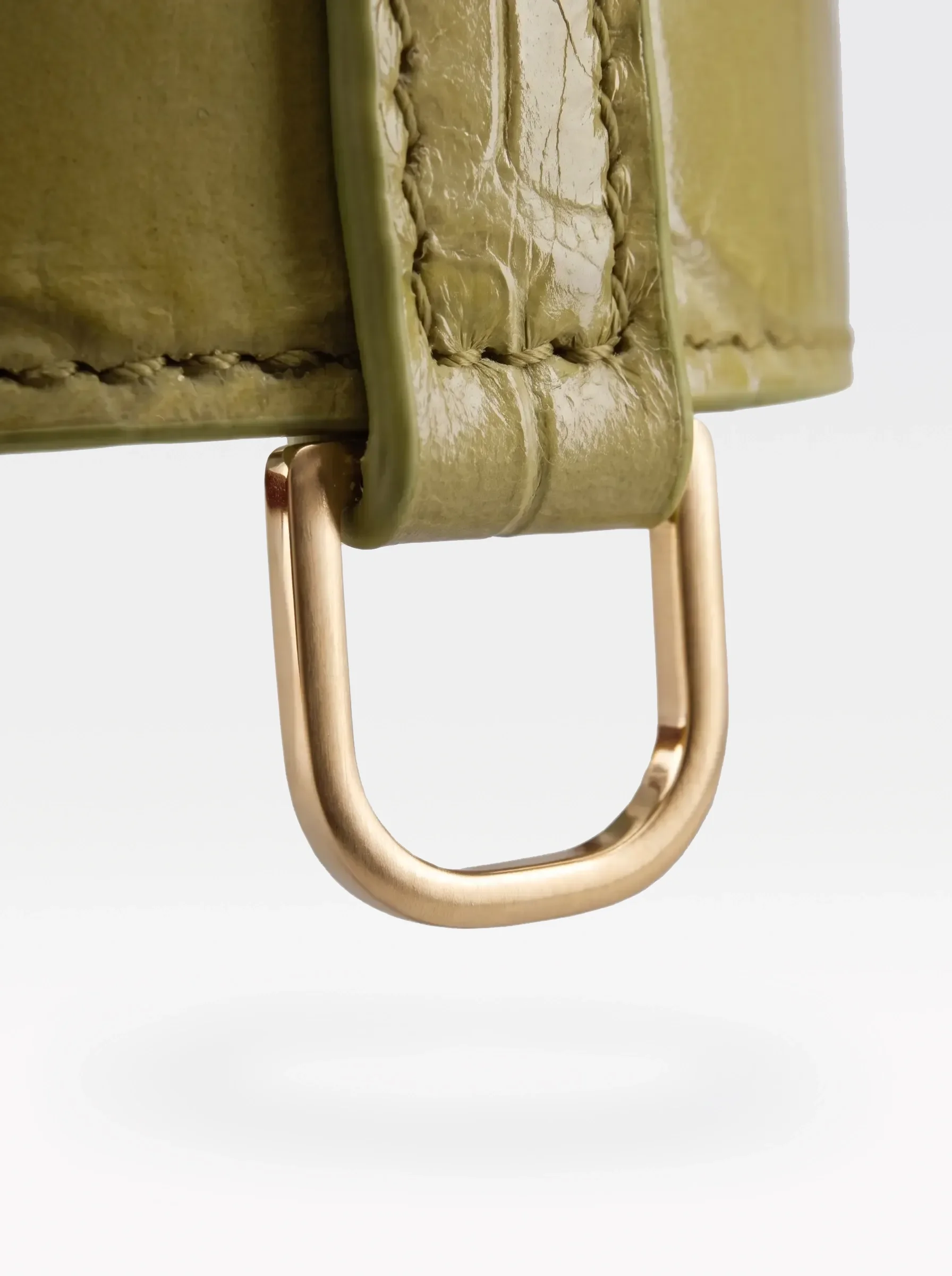Close-up of the 24K gold-plated brass D ring on a pistachio crocodile-embossed lambskin choker by Sainte Sve