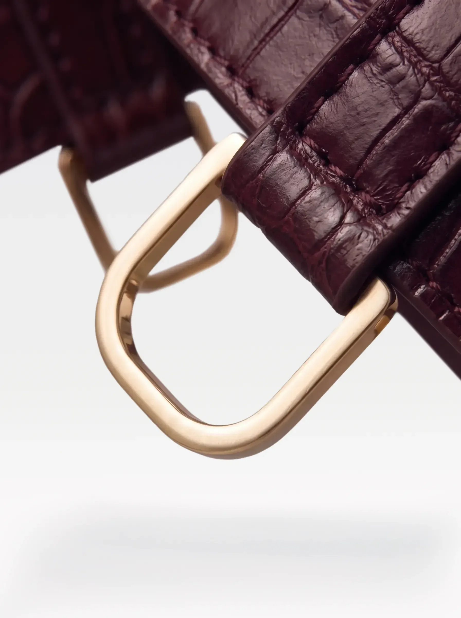 Close-up of the 24K gold-plated brass D ring on a burgundy crocodile-embossed lambskin garter by Sainte Sve