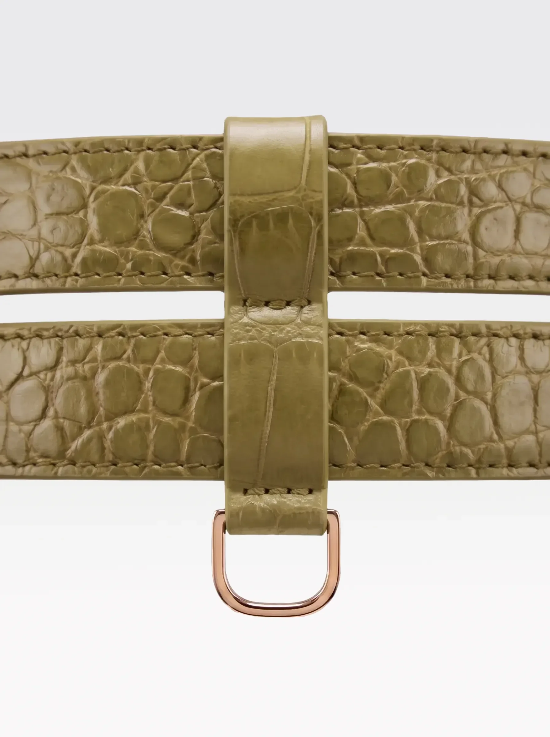Close-up of the 24K gold-plated brass D ring on the pistachio crocodile-embossed lambskin double band of the Sainte Sve Belt Croc