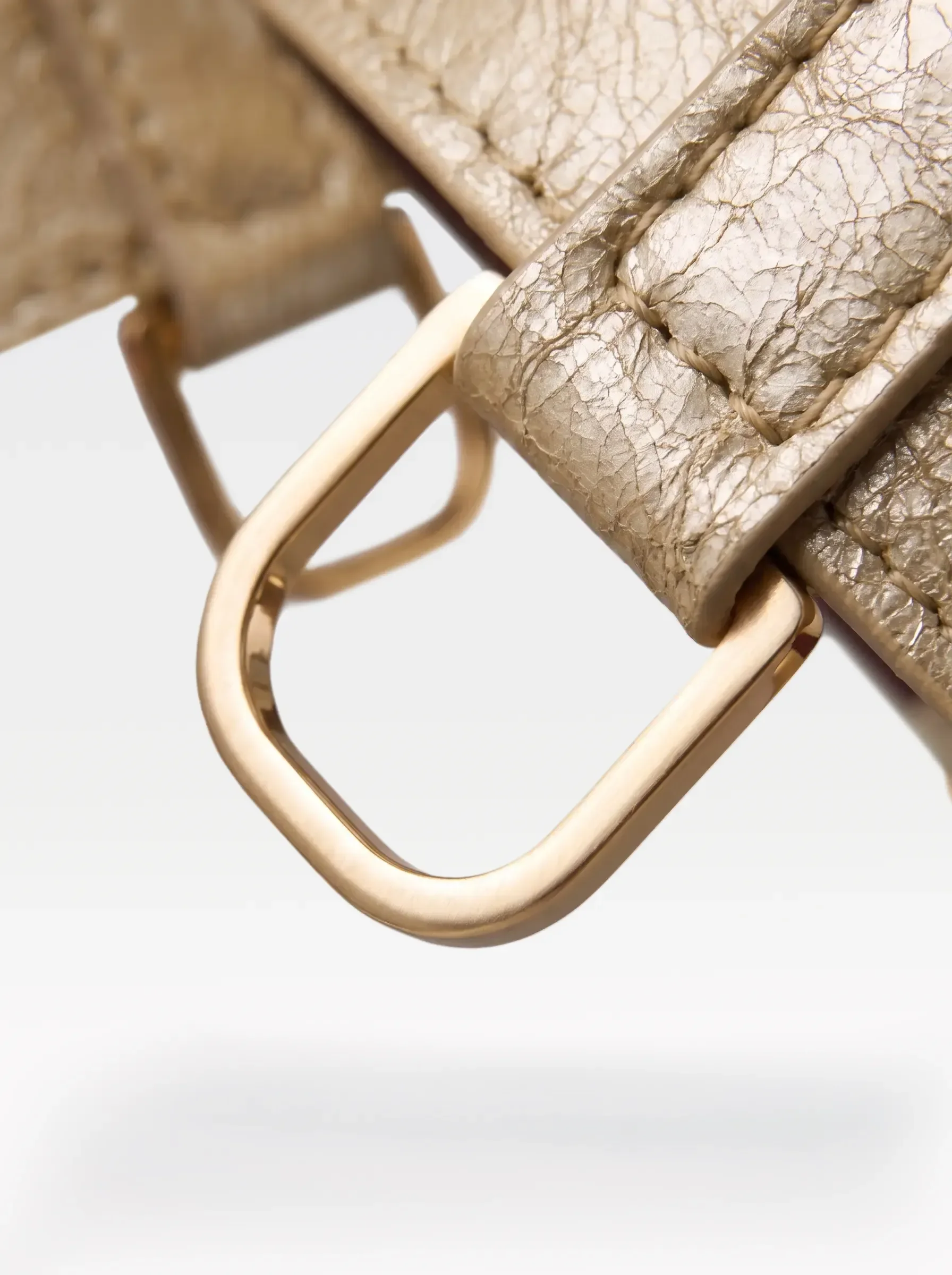 Close-up of the 24K gold-plated brass D ring on a gold laminated lambskin garter by Sainte Sve