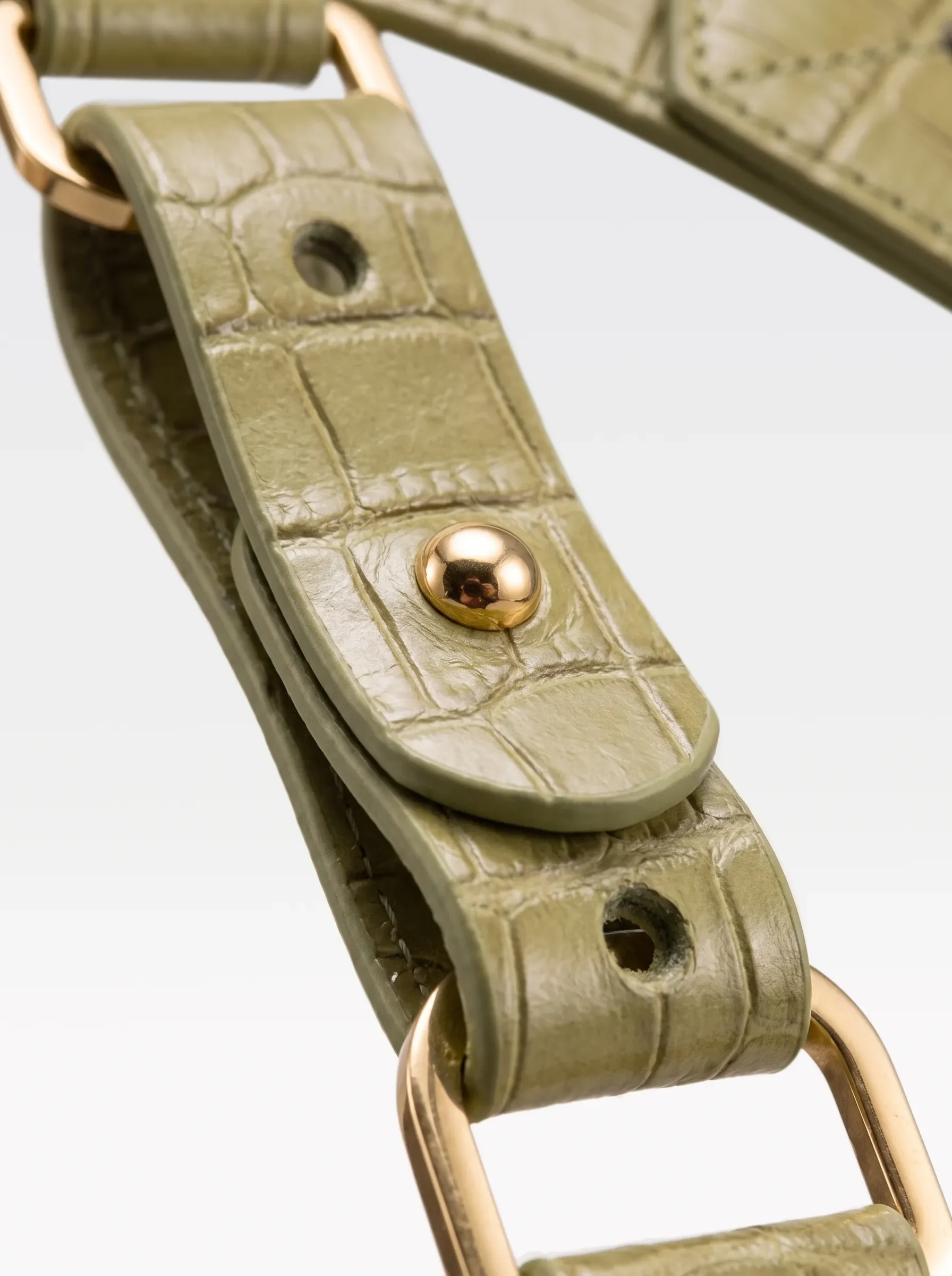 Close-up of the 24K gold-plated brass connector rivet and D ring on the pistachio crocodile-embossed lambskin strap of the Sainte Sve Belt Plus Croc