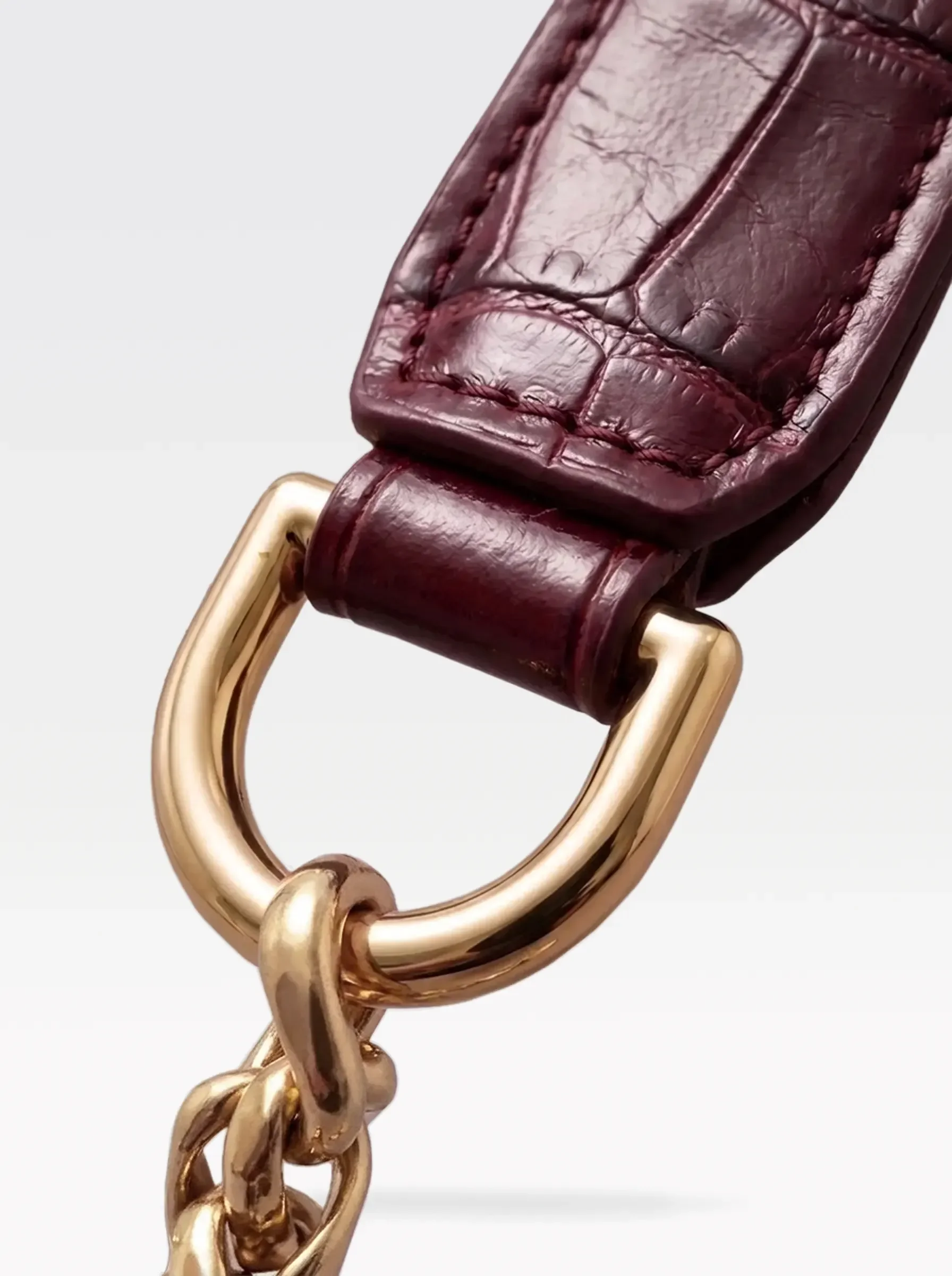 Close-up of the 24K gold-plated brass D ring joining the burgundy crocodile-embossed lambskin handle to the chain of the Sainte Sve Leash Croc