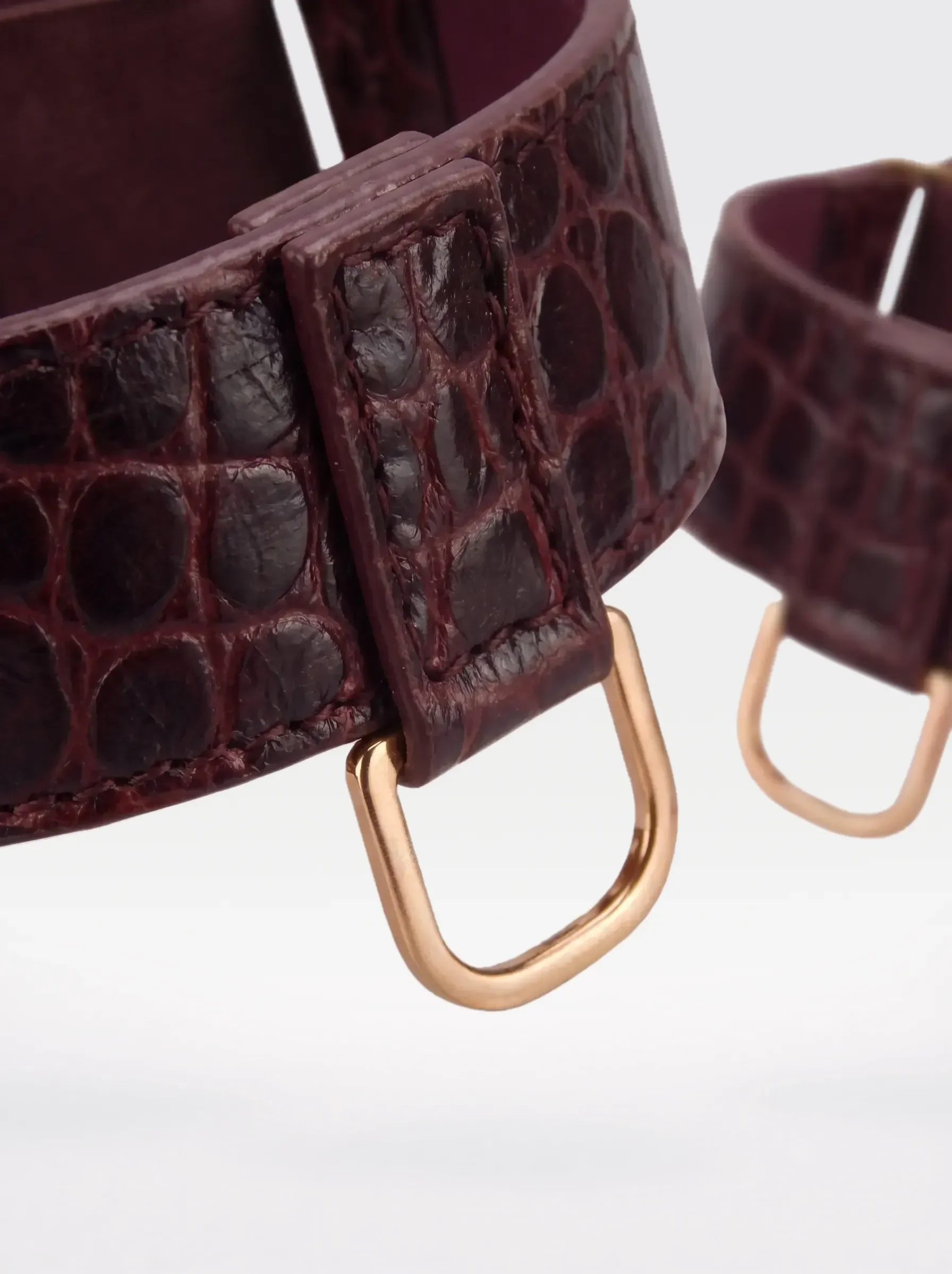 Close-up of the 24K gold-plated brass D ring on a burgundy crocodile-embossed lambskin arm bracelet by Sainte Sve