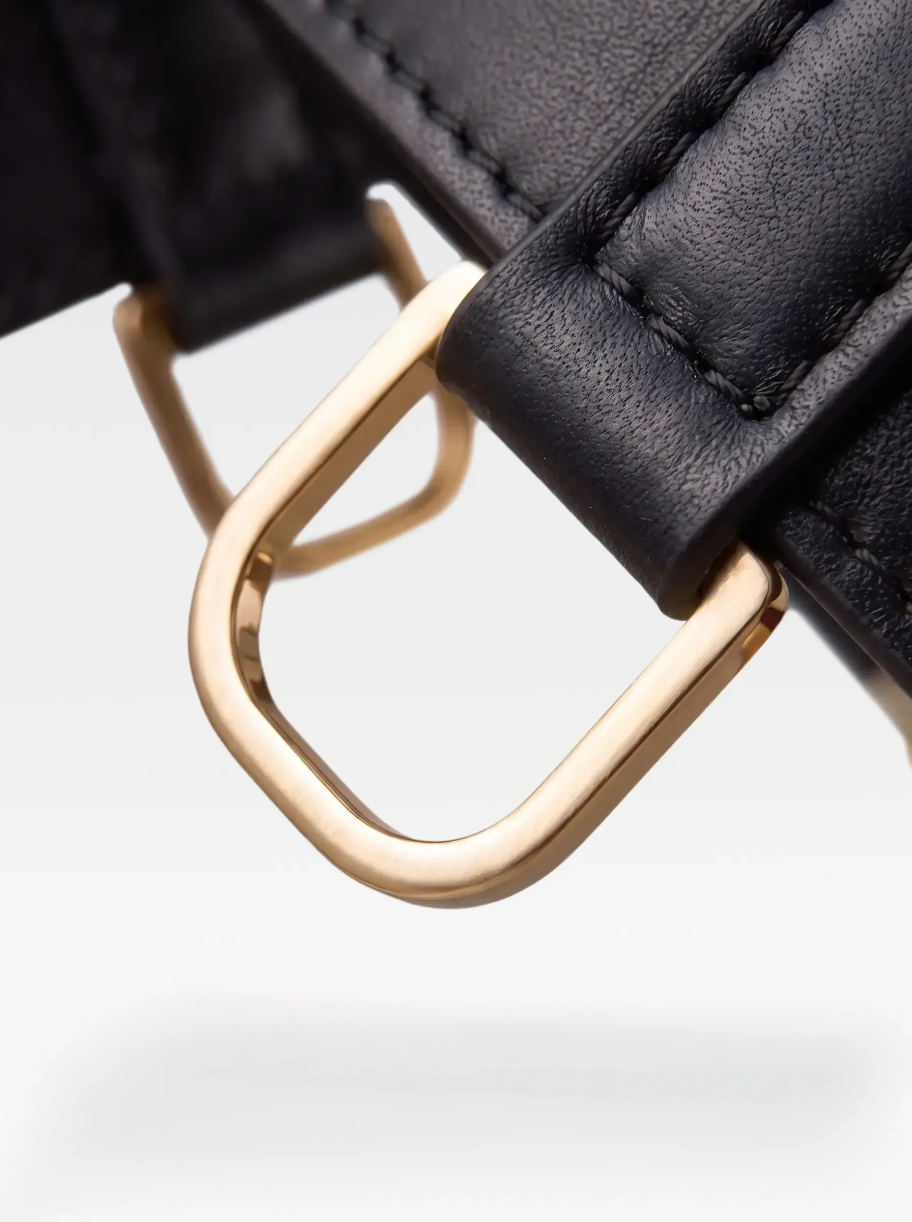 Close-up of the 24K gold-plated brass D ring on a black nappa lambskin garter by Sainte Sve