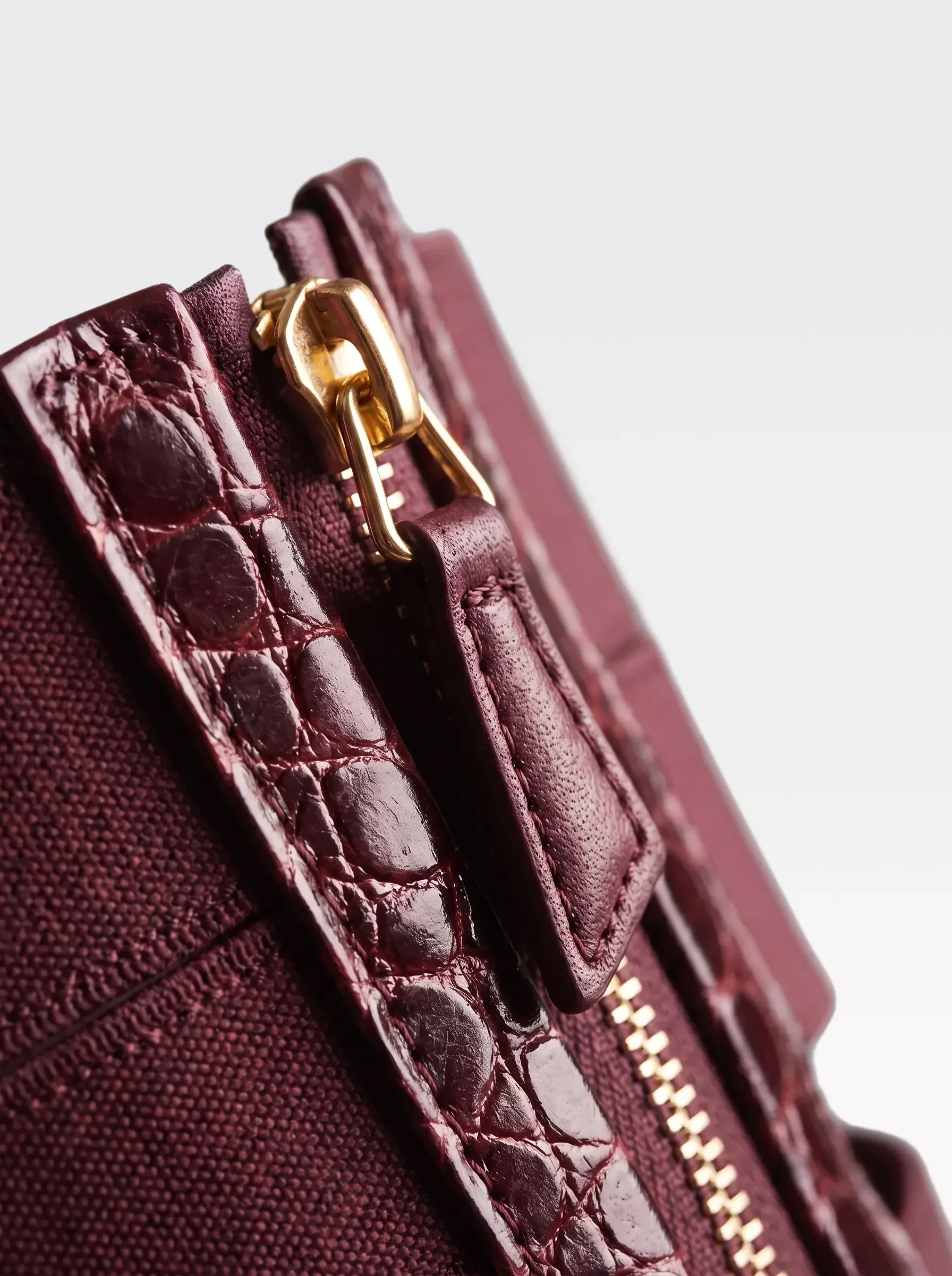Close-up of the 24K gold-plated brass zip on the burgundy crocodile-embossed lambskin of the Sainte Sve V.N.V Croc