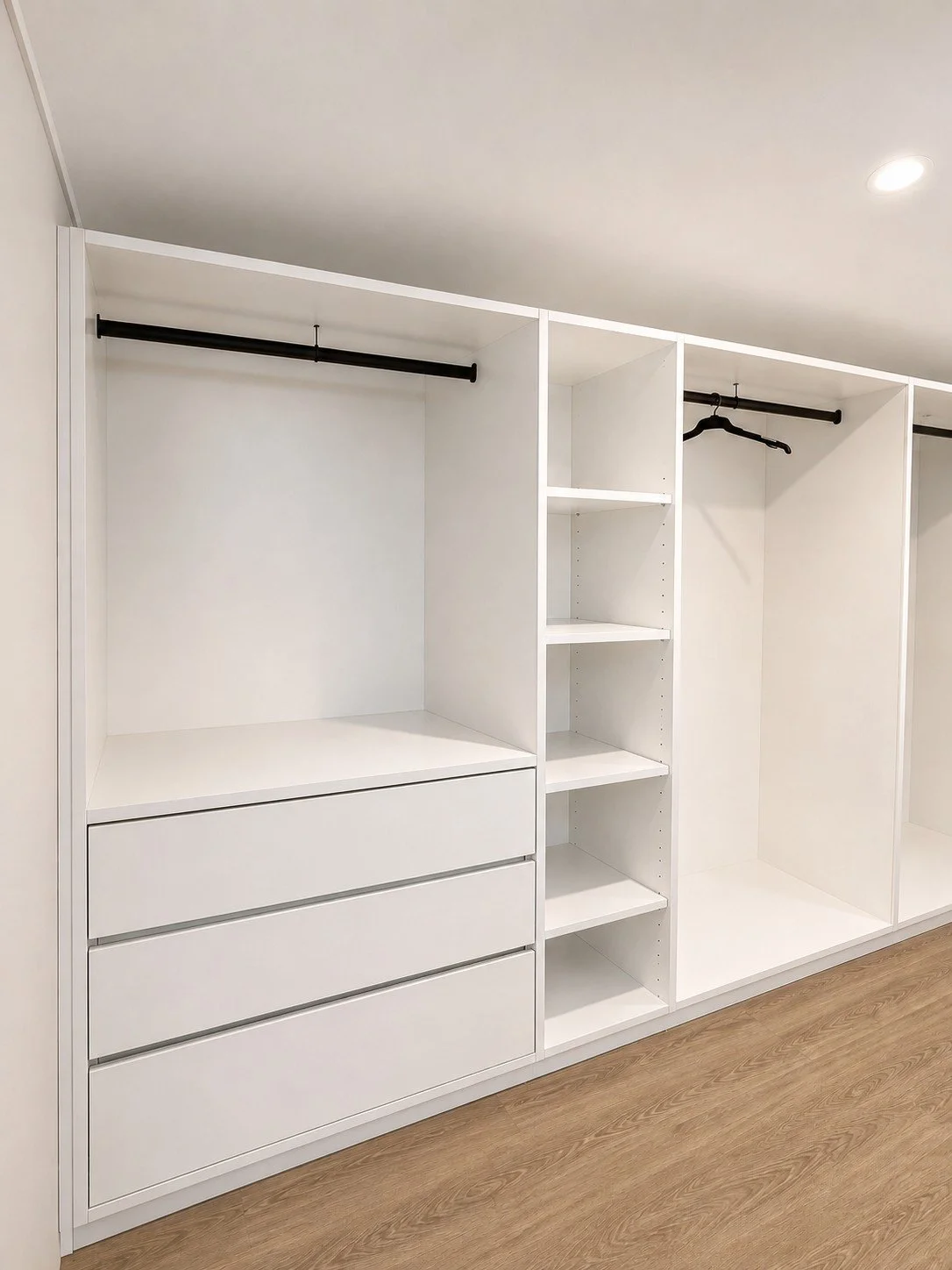 Empty white closet organizer with drawers, shelves, and hanging rods on a wooden floor.