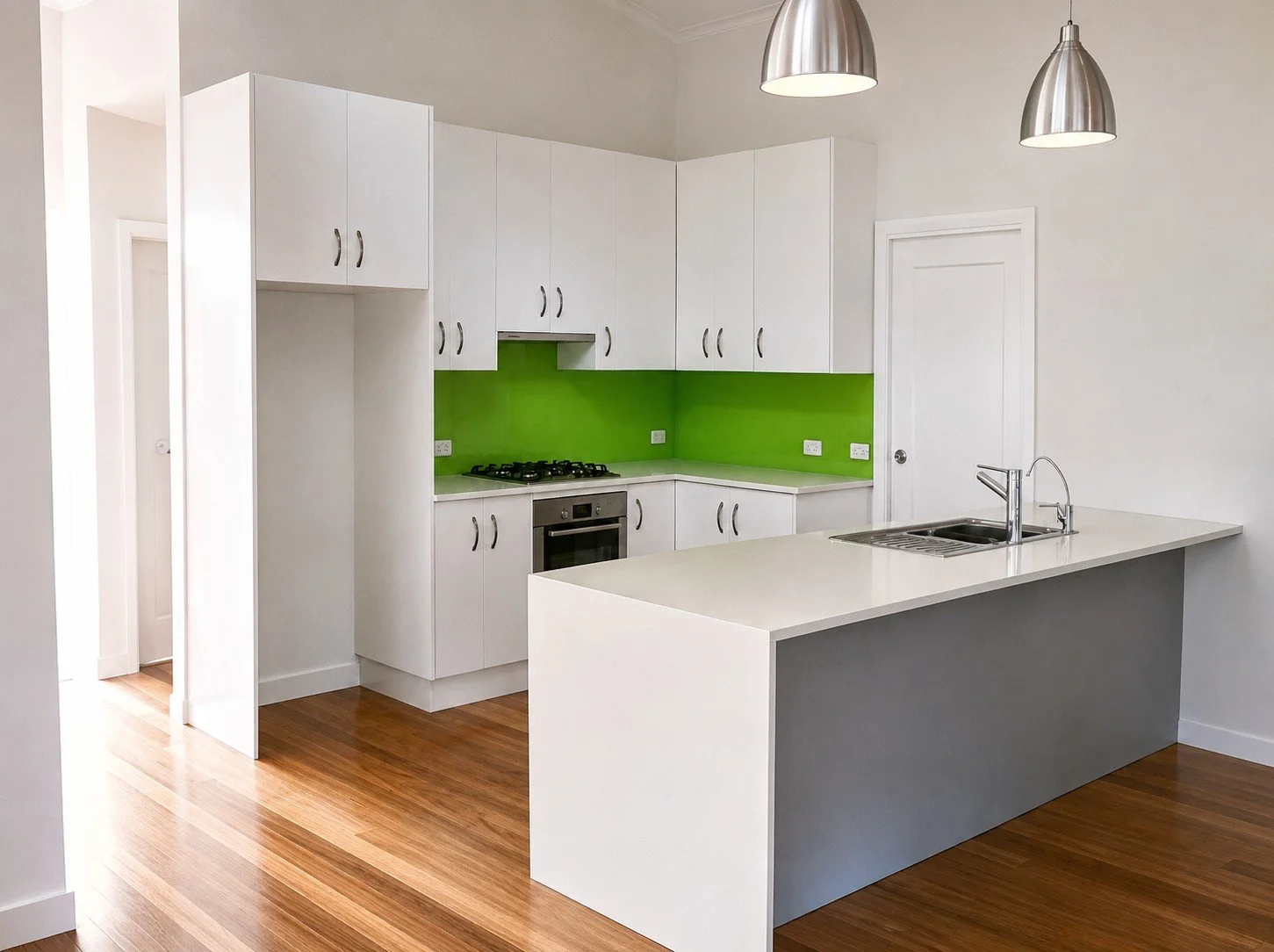 Modern kitchen with white cabinets, a green glass splashback, a kitchen island with a sink, and stainless steel pendant lights.