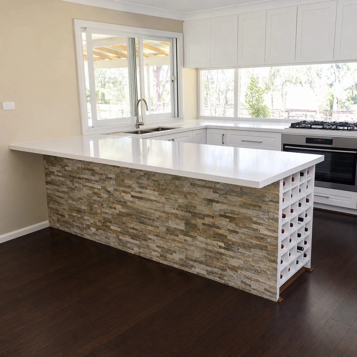 Custom white kitchen with stone feature island, integrated wine storage and detailed cabinetry.
