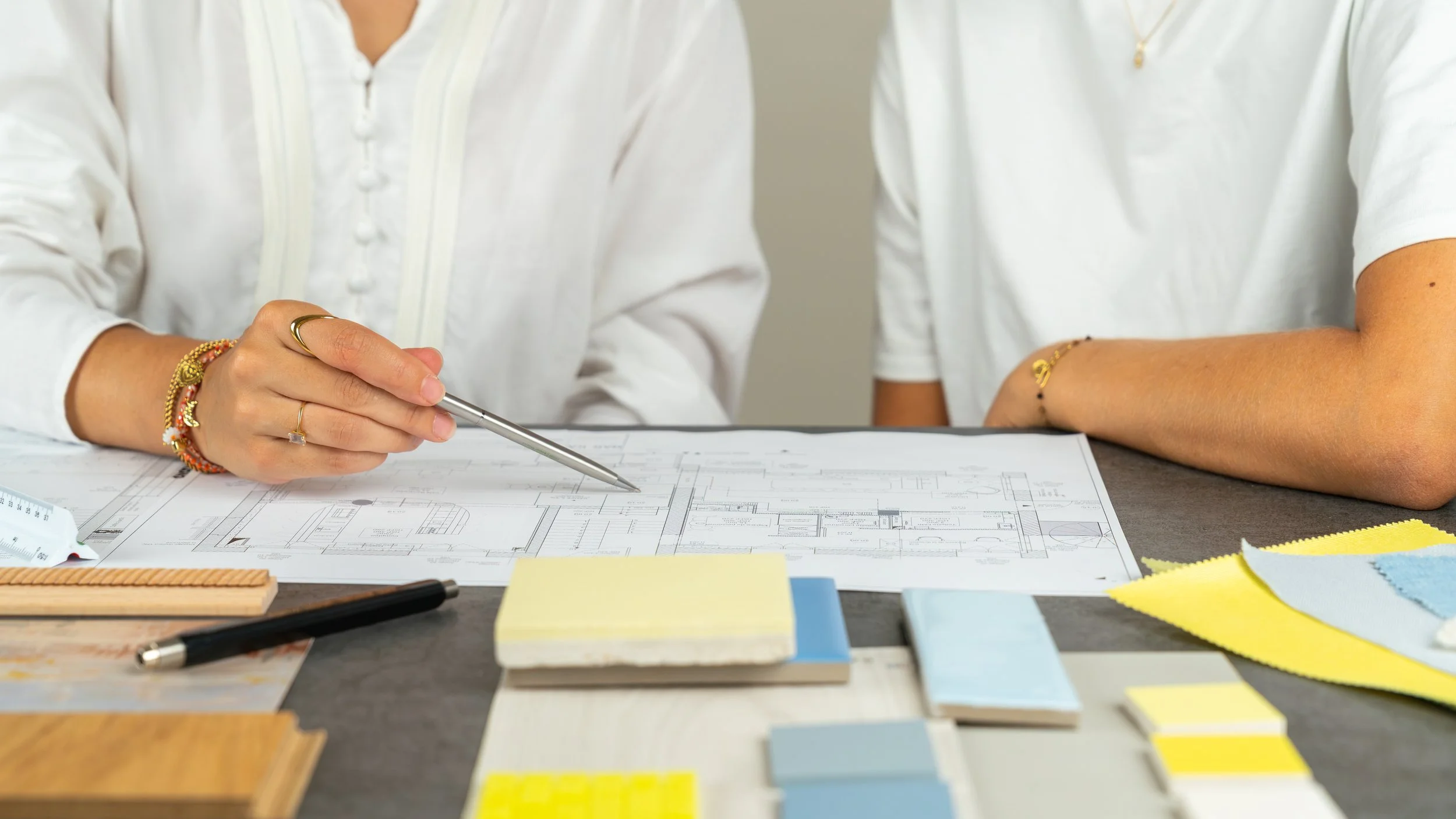 Deux personnes travaillant sur un projet d’architecture intérieure, autour d’un plan et d’échantillons de matériaux.