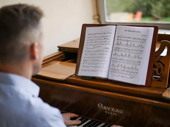 Une personne joue du piano, ses mains sur les touches, avec une partition ouverte sur le support du piano.