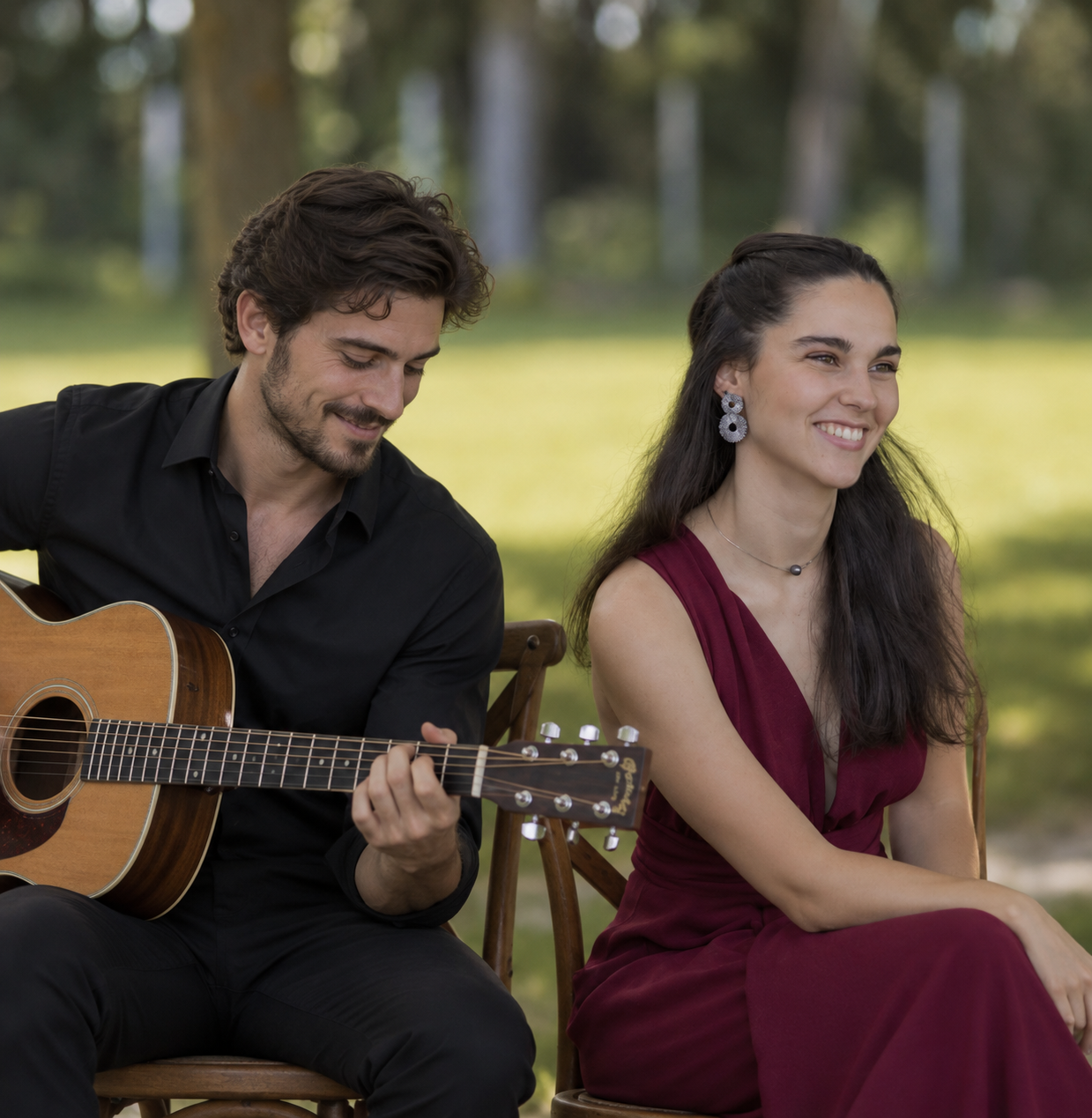 Un homme et une femme assis sur des chaises en bois dans un parc, l'homme joue de la guitare et la femme sourit, ambiance détendue et ensoleillée.