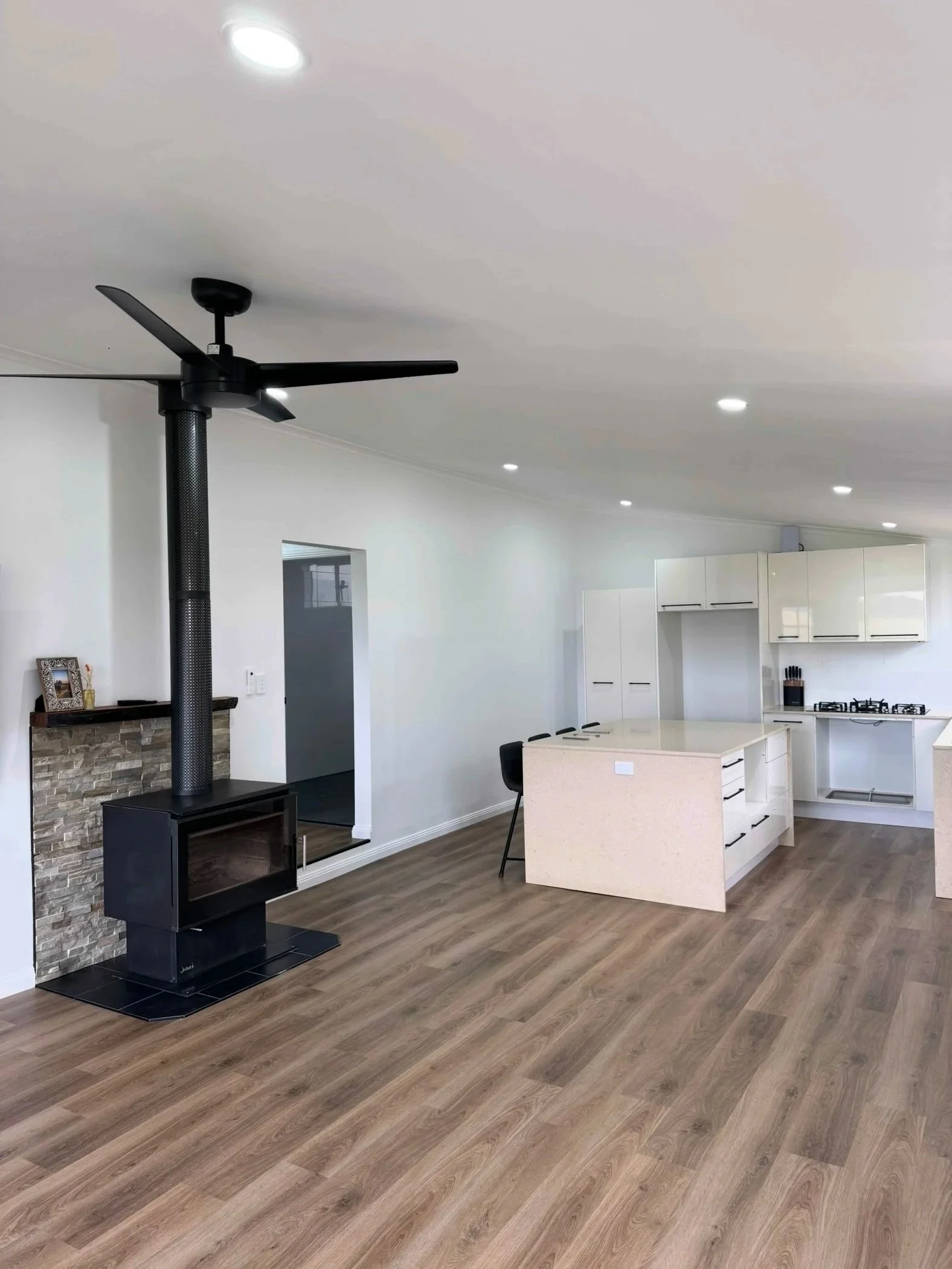 Modern, open-concept kitchen and living space with a black wood-burning stove, white cabinets, a kitchen island, and wood-look flooring.