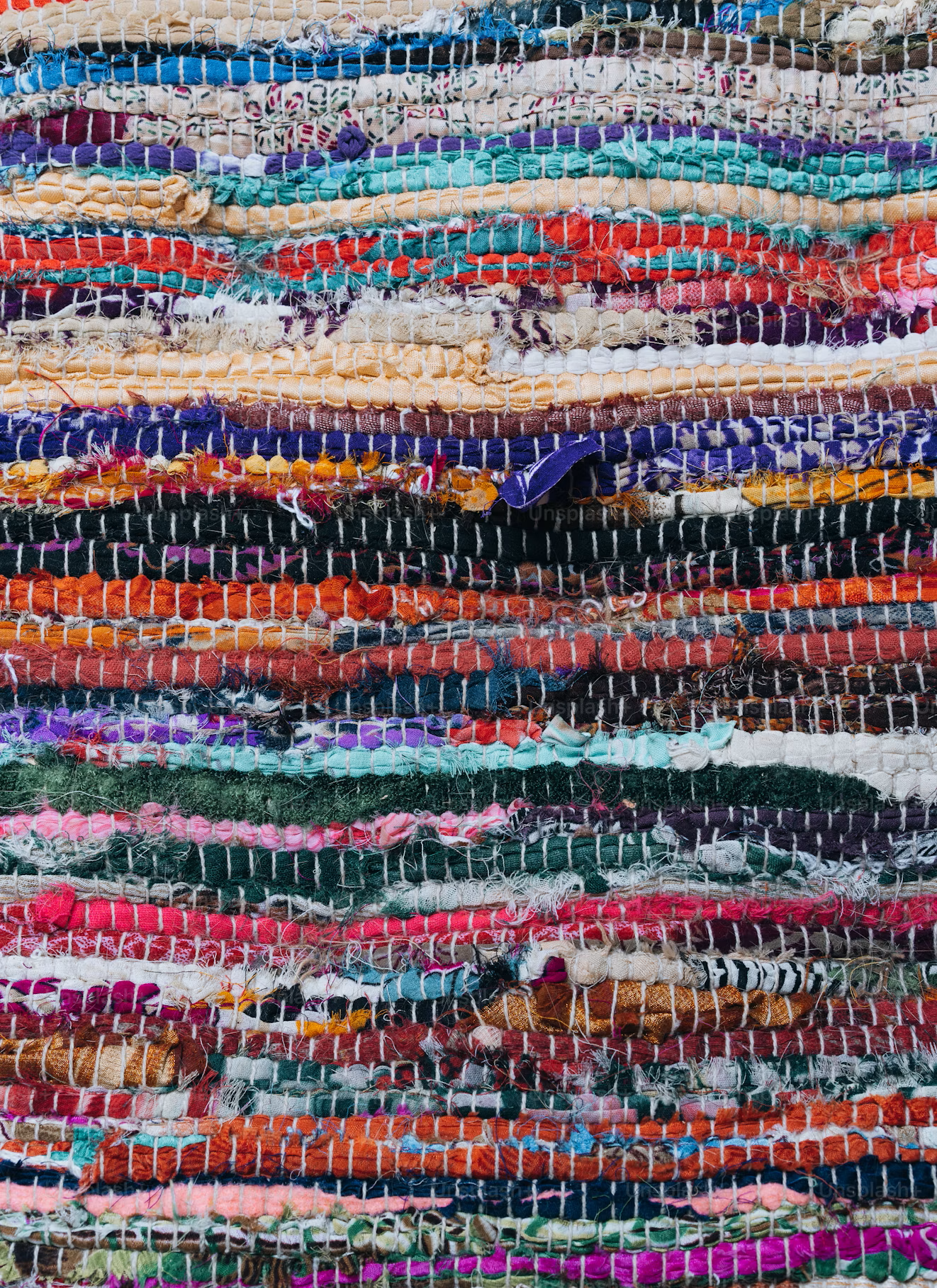 A pile of colorful woven textiles and rugs stacked horizontally.