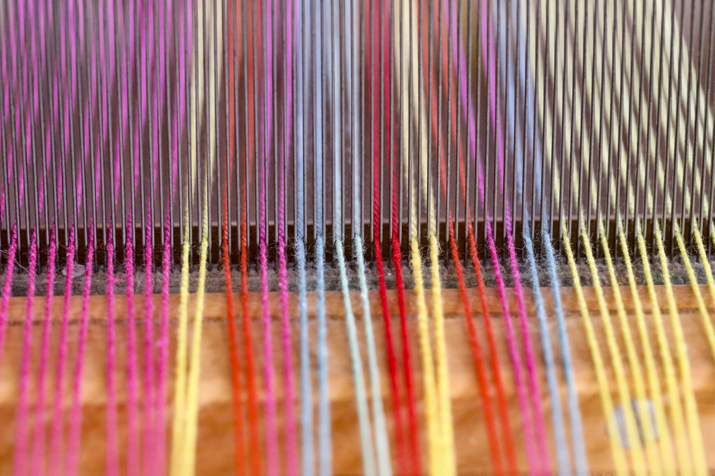 Close-up of colorful embroidery threads stretched on a wooden loom.