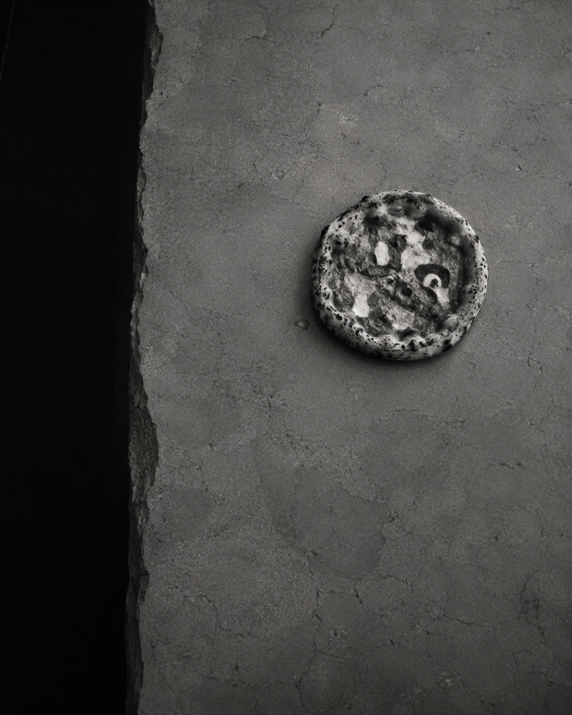 Black-and-white editorial image of a small pizza on a textured surface, accompanying The Little Helper’s strategy-first marketing approach.