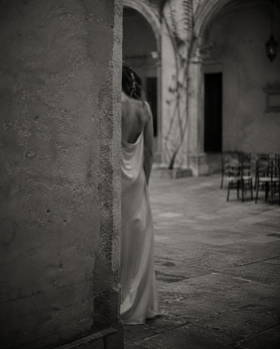 Black-and-white editorial image of a woman in a long dress standing beside chairs, accompanying The Little Helper’s strategic marketing content.