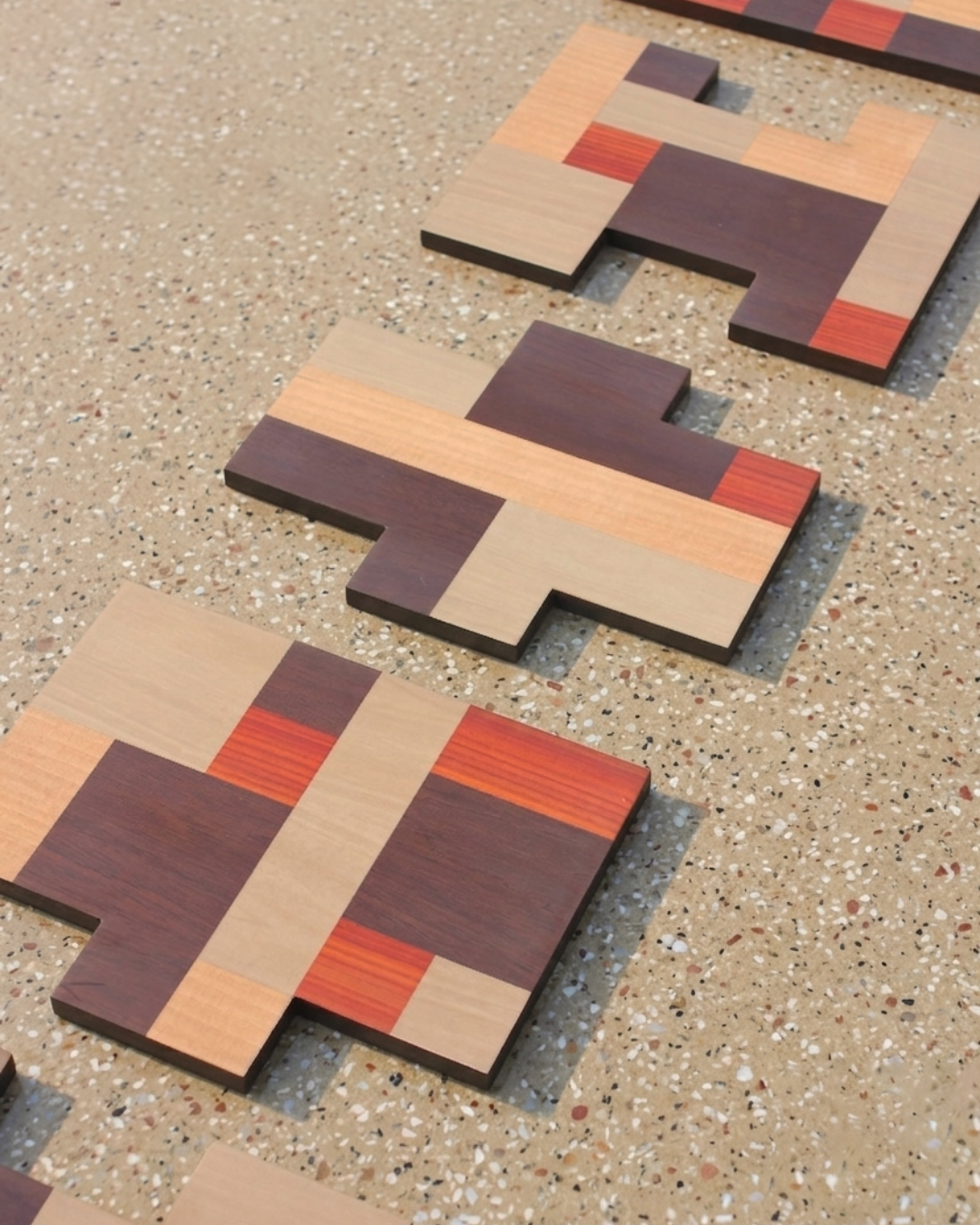 Three wooden puzzle pieces with colorful horizontal stripes, placed on a terrazzo floor.