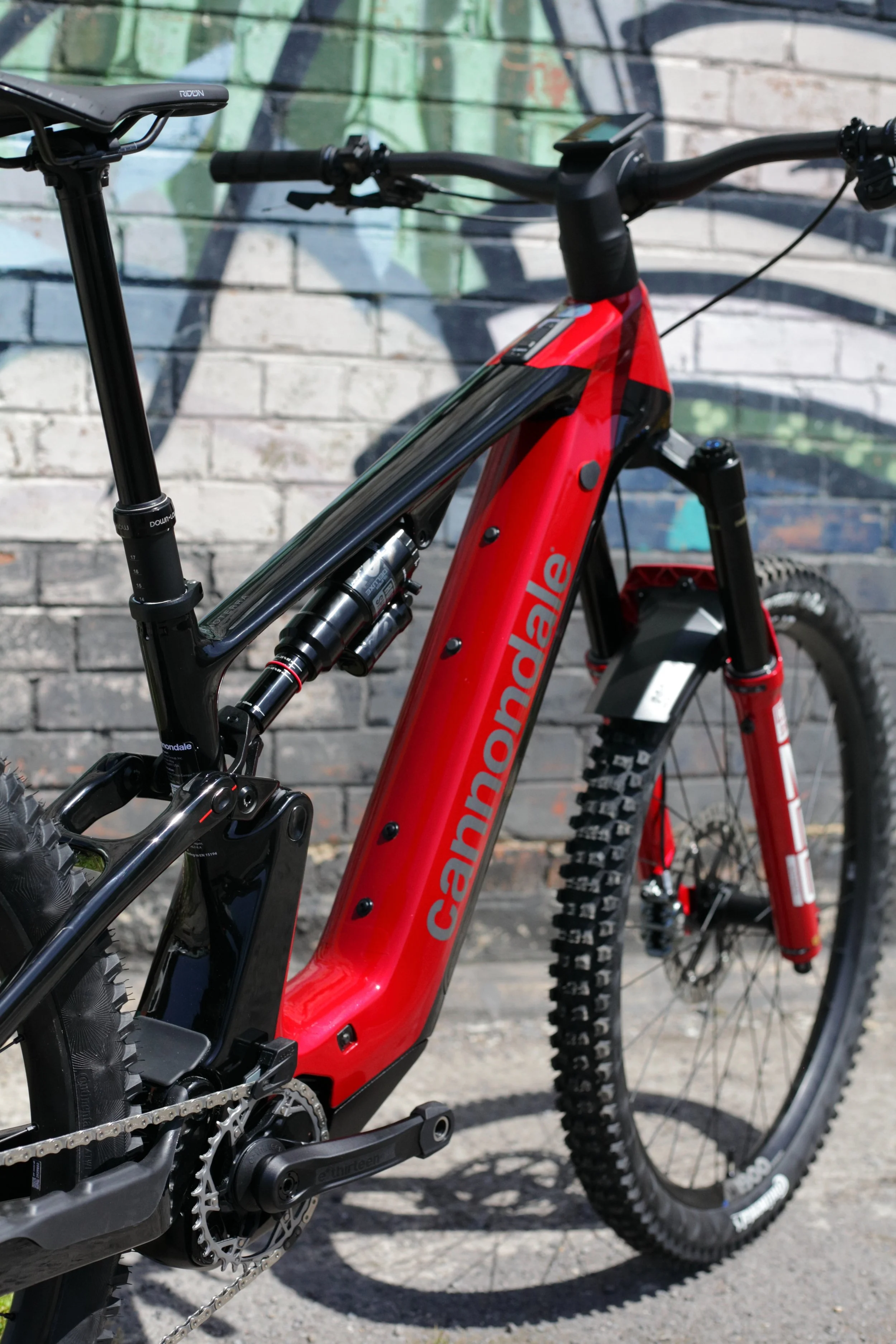 Close-up of a red Canyon mountain bike with black suspension, resting against a brick wall with graffiti.