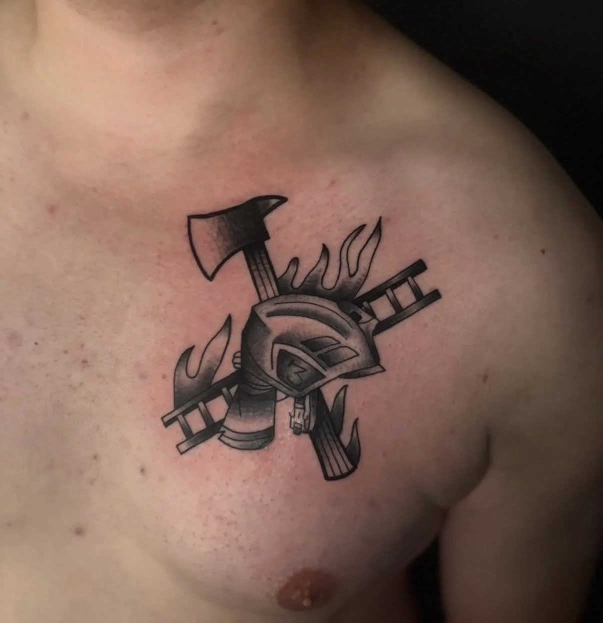 Tattoo eines Helms mit zerbrochenen Waffen und Flammen auf der Brust