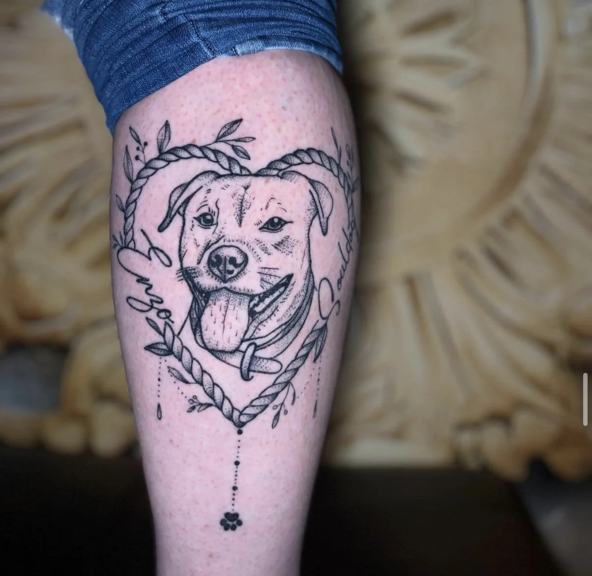 Schwarz-weiße Hundetattoo auf der Wade, umgeben von einer Herzform aus Seilen, mit Namen und Dekorationen.