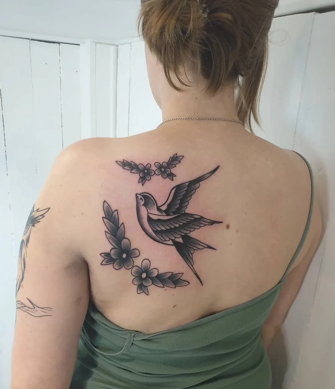 Schultertattoo eines fliegenden Vogels mit Blumen und Blättern.